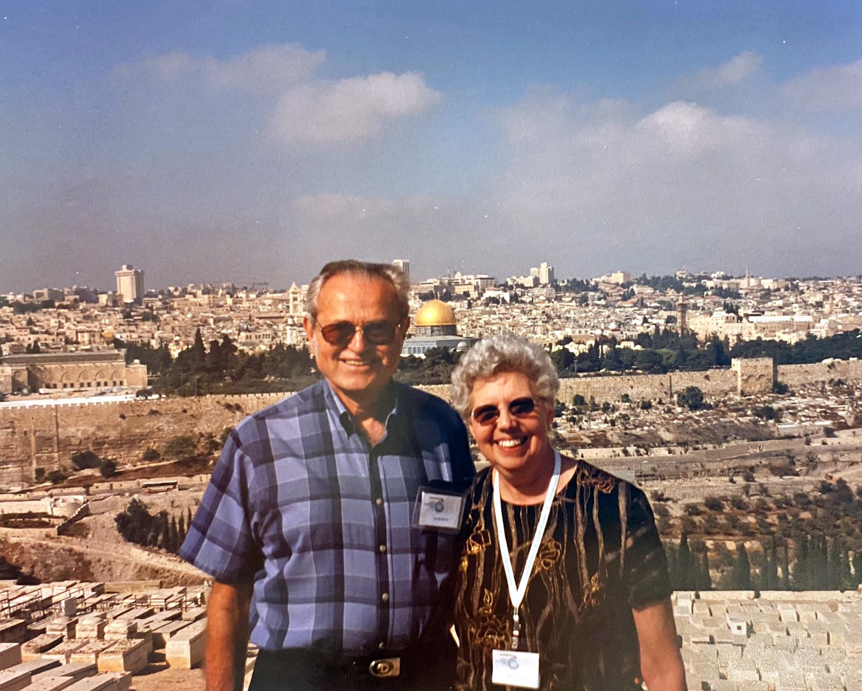 A happy couple poses with Jerusalem’s historic skyline in the background on a sunny day.