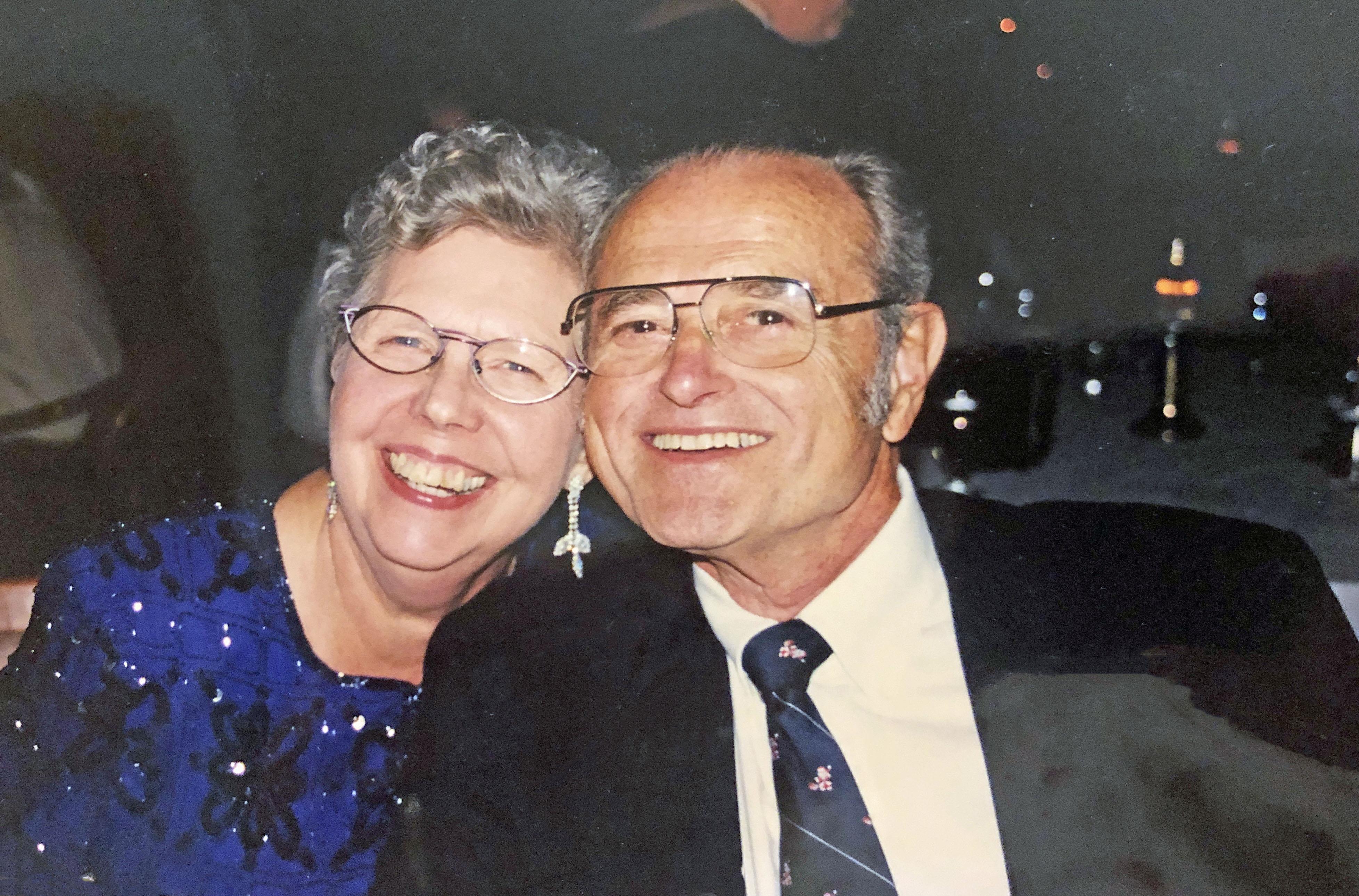 A joyful couple smiles together at a festive family gathering, celebrating their love.
