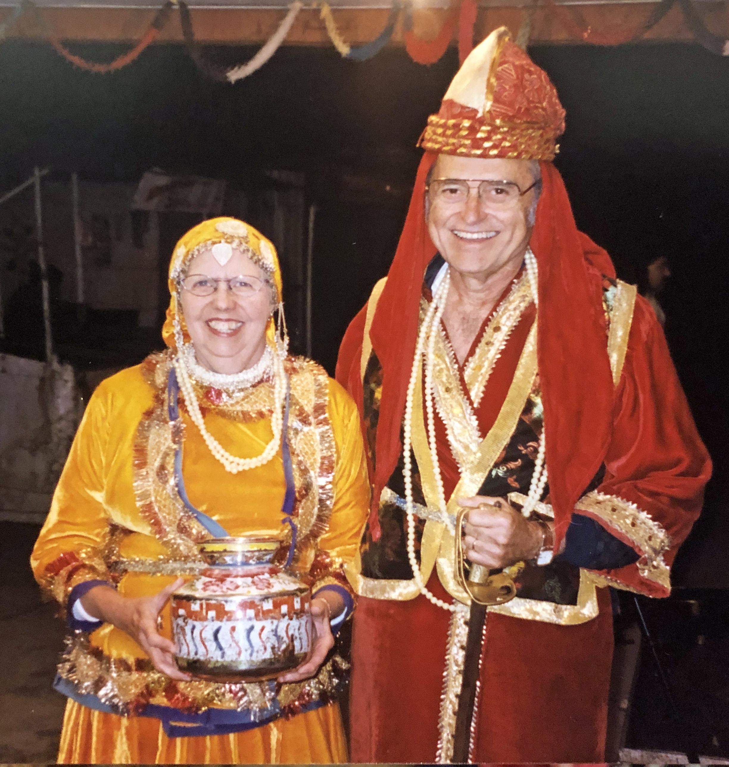 Elderly couple in bright traditional costumes joyfully shares smiles at a cultural festival.