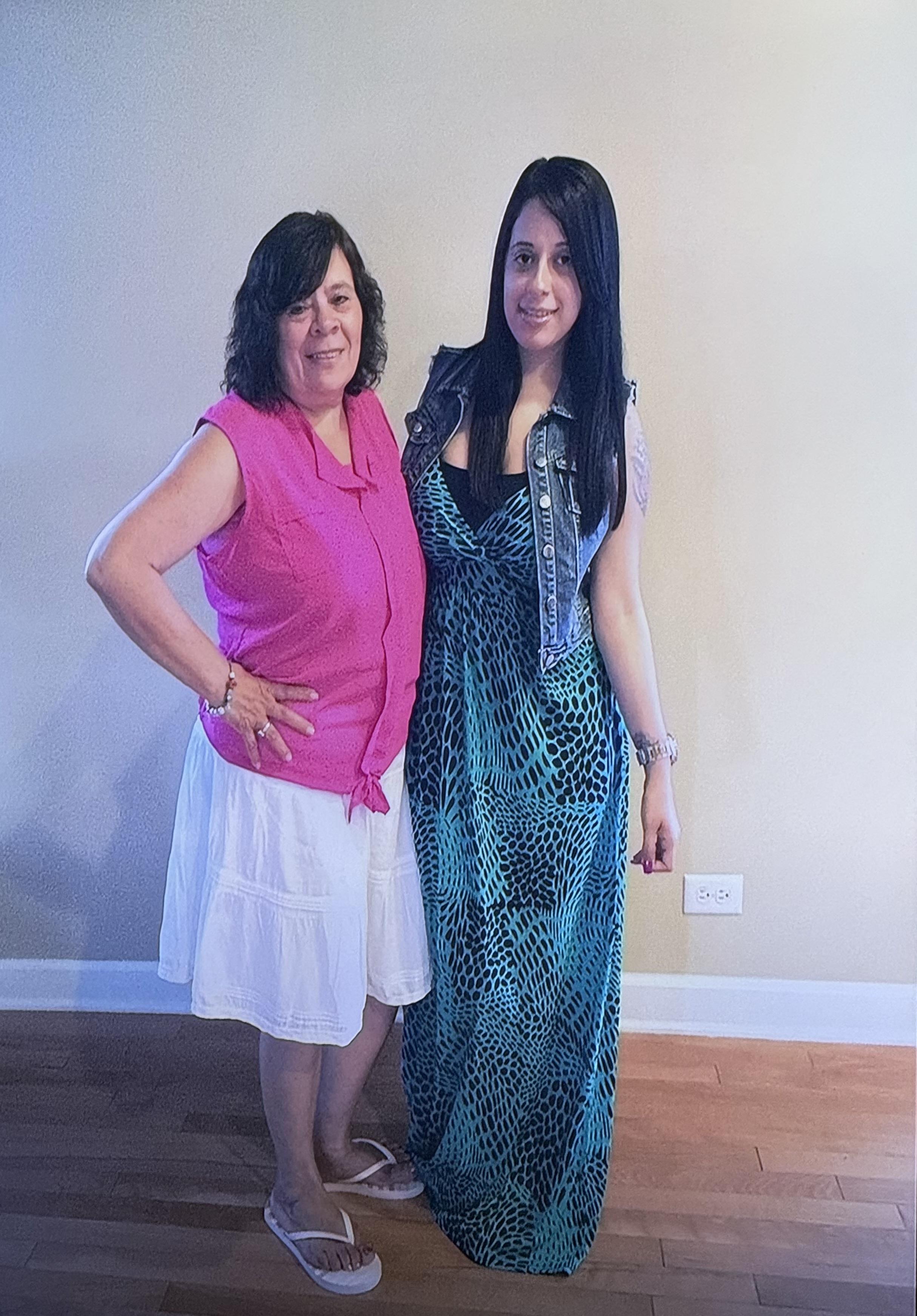 Two women show off their stylish outfits and joyful smiles in a living room.
