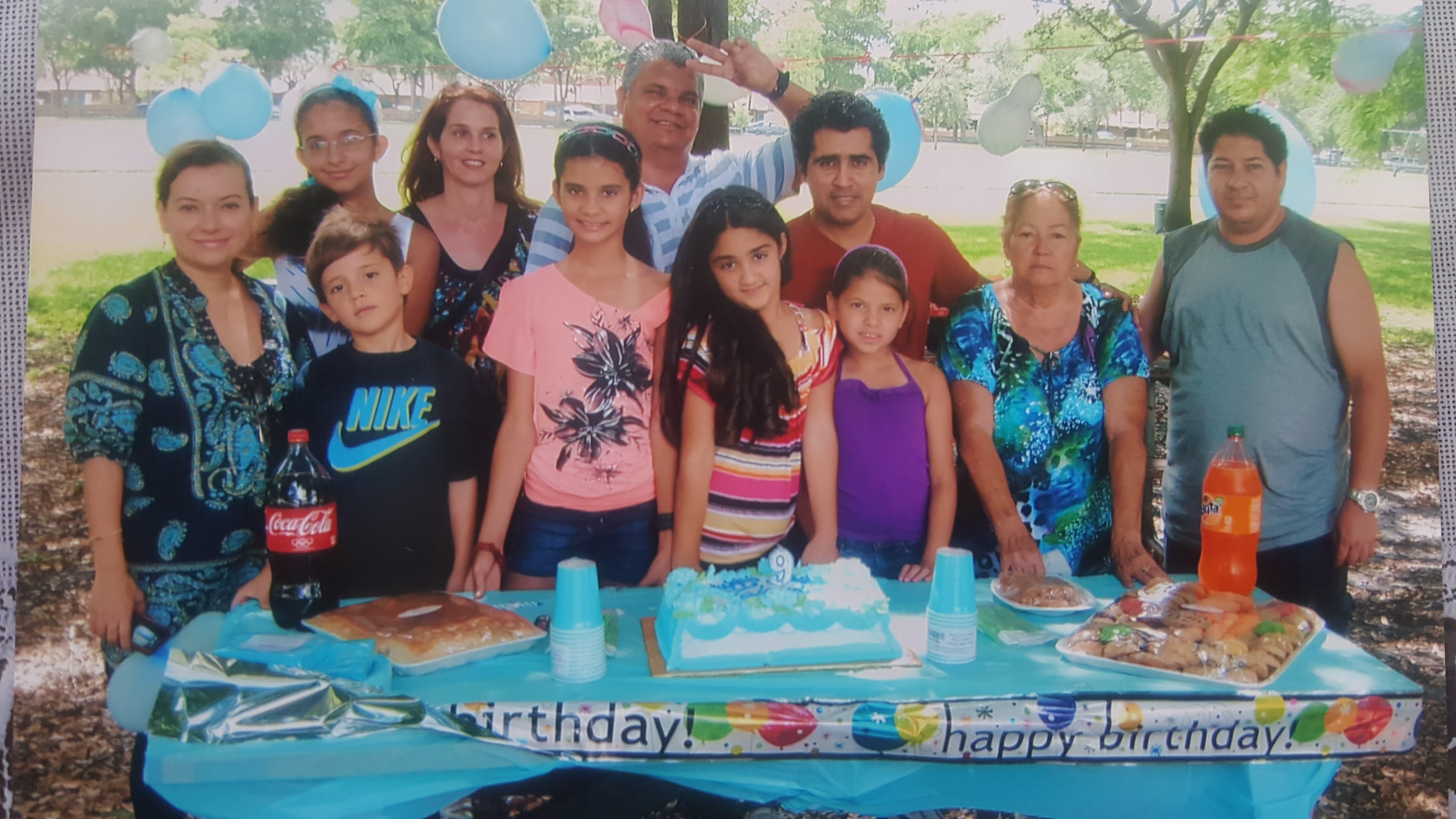 A happy family celebrates a birthday with cake and decorations in a park.