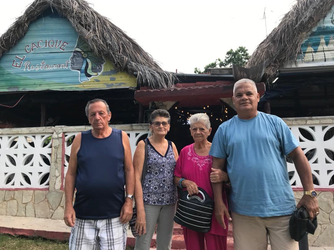 Friends gather outside a traditional building with thatched roofs, enjoying their time together.