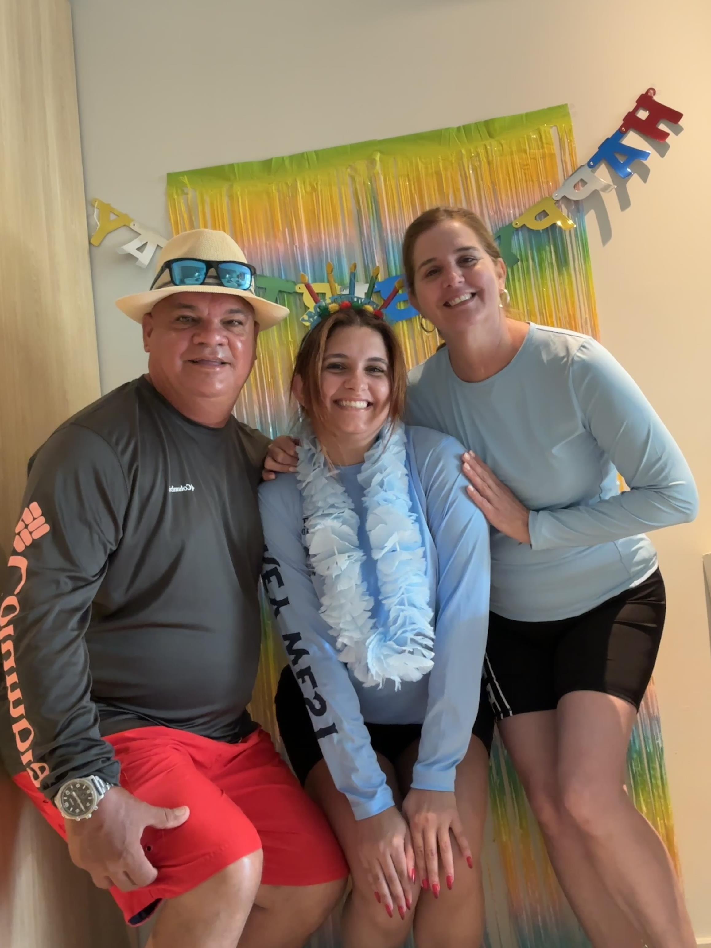Three friends pose happily at a beach-themed celebration adorned with colorful decorations.