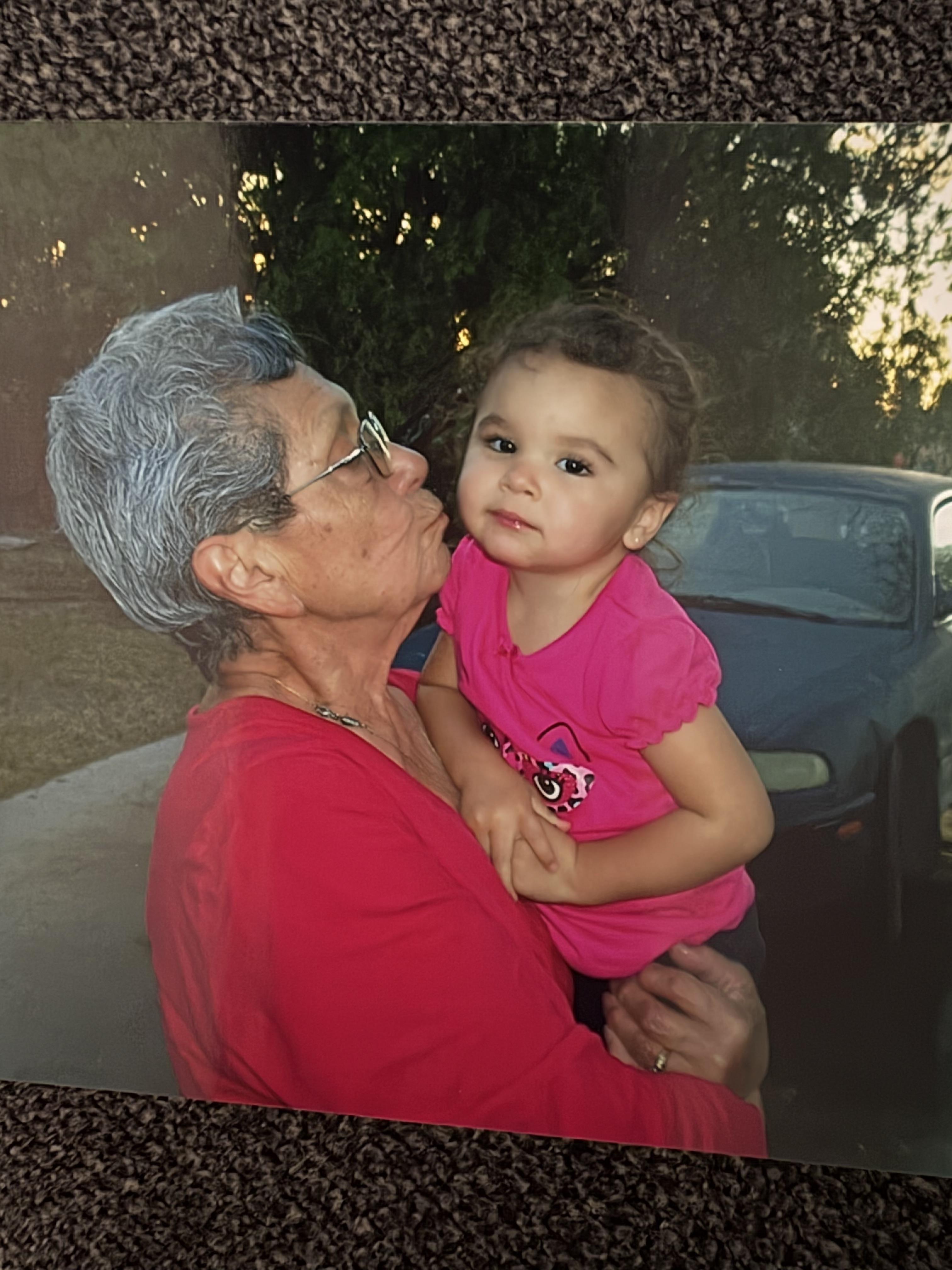 A grandmother gives a gentle kiss to her granddaughter while holding her outside at sunset.