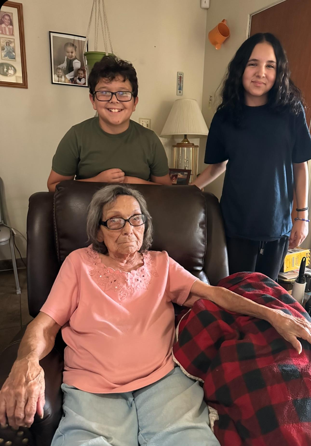 Two children stand beside a grandmother seated in a cozy living room, sharing heartfelt smiles.