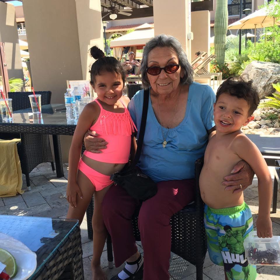 Two children pose with their grandmother at a sunlit outdoor resort area beside a pool.