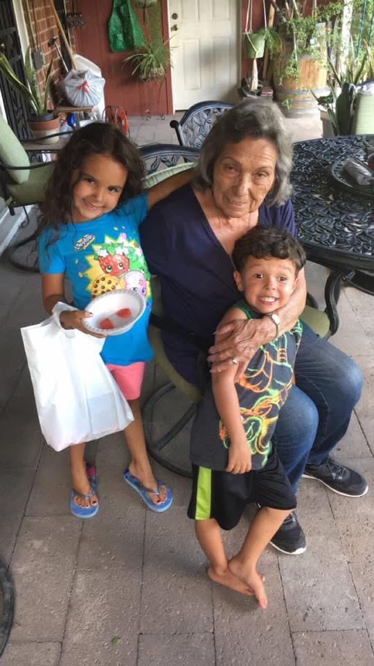 Two children smile while holding snacks next to an elderly woman at home, sharing joy and laughter.