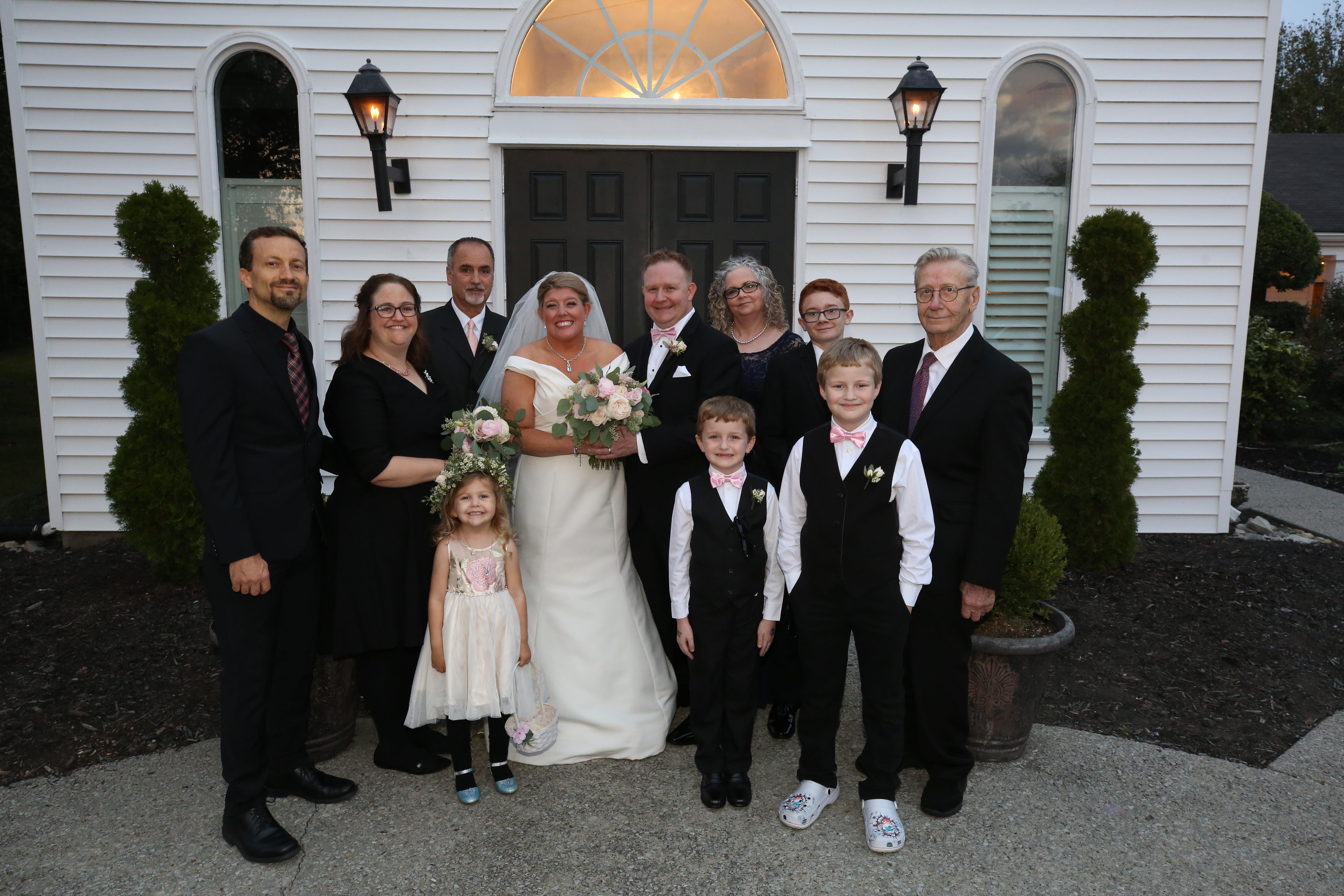 Family and friends gather joyfully for a wedding celebration outside a lovely venue at dusk.