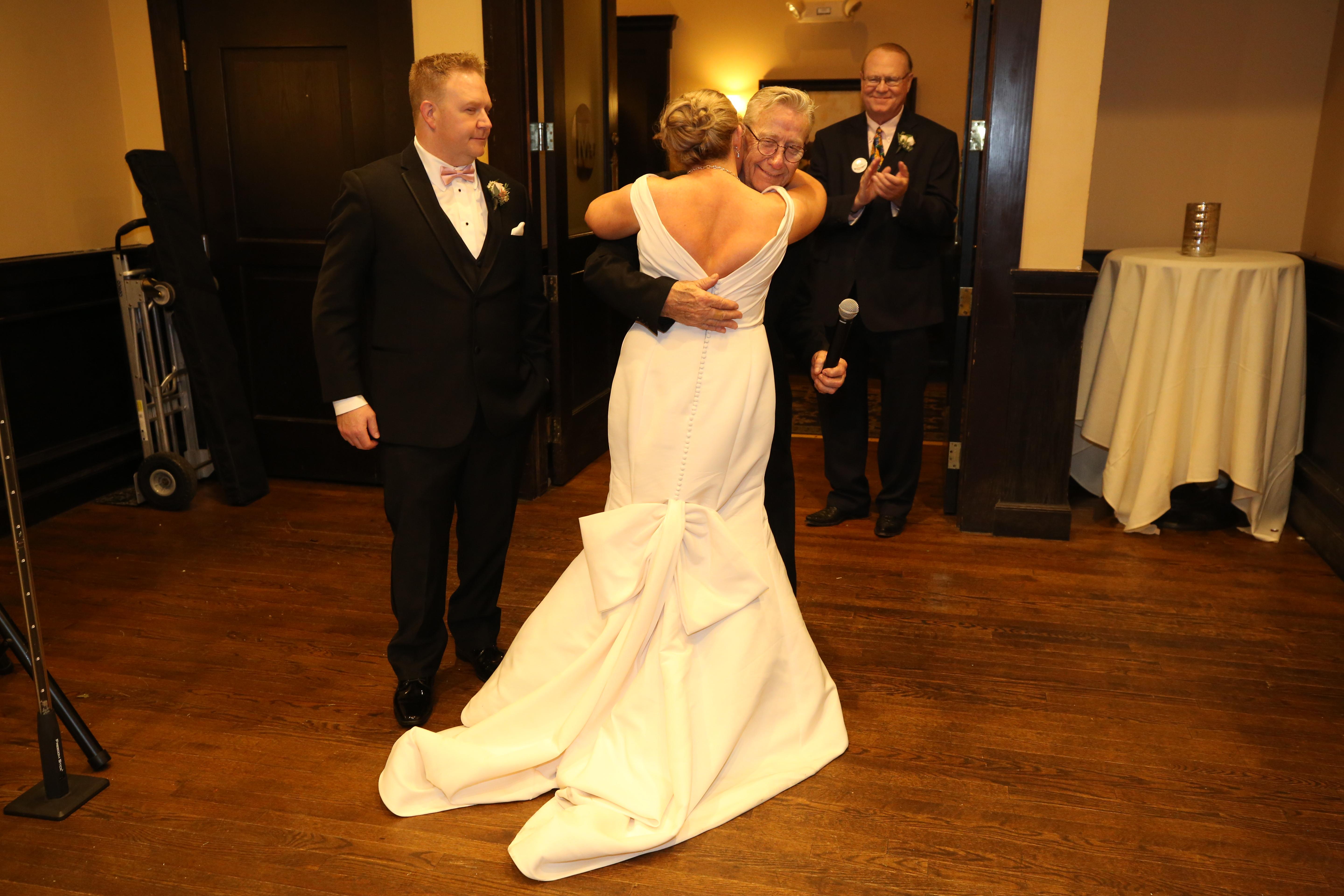 A joyous couple embraces at their wedding reception while guests applaud and celebrate the moment.
