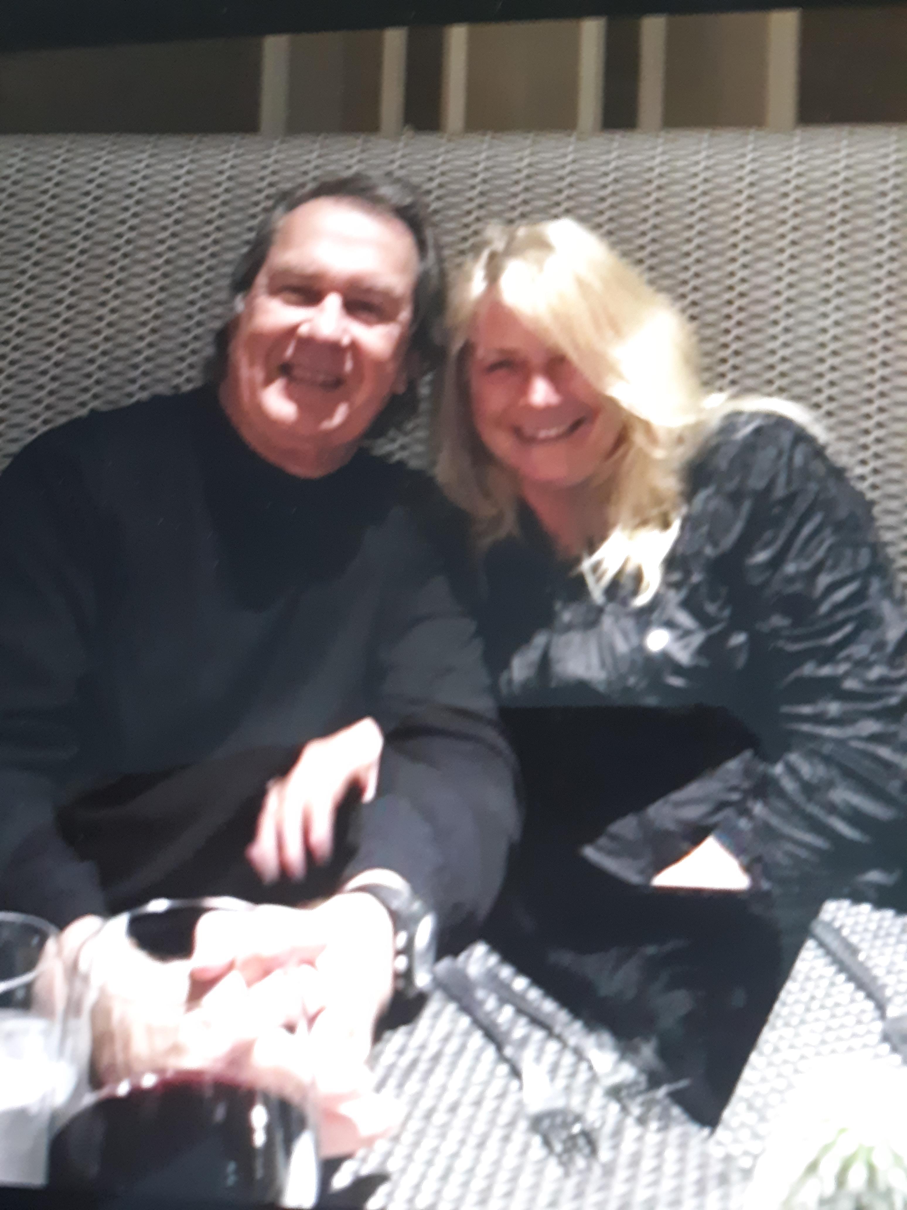 Two smiling individuals sit closely together at a stylish dining venue, sharing a joyful moment.