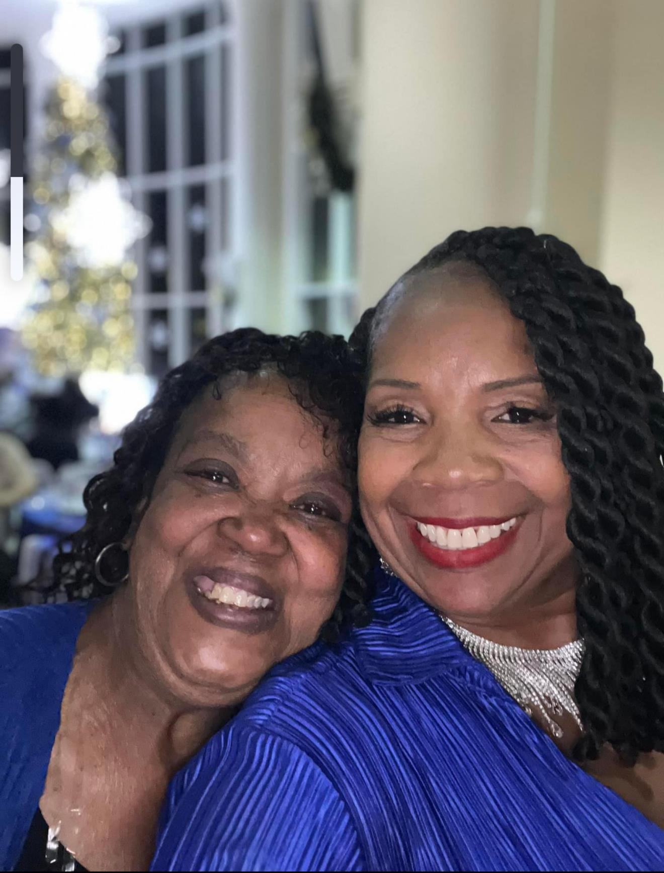 Two women share a joyful moment, displaying bright smiles at an event filled with decorations.