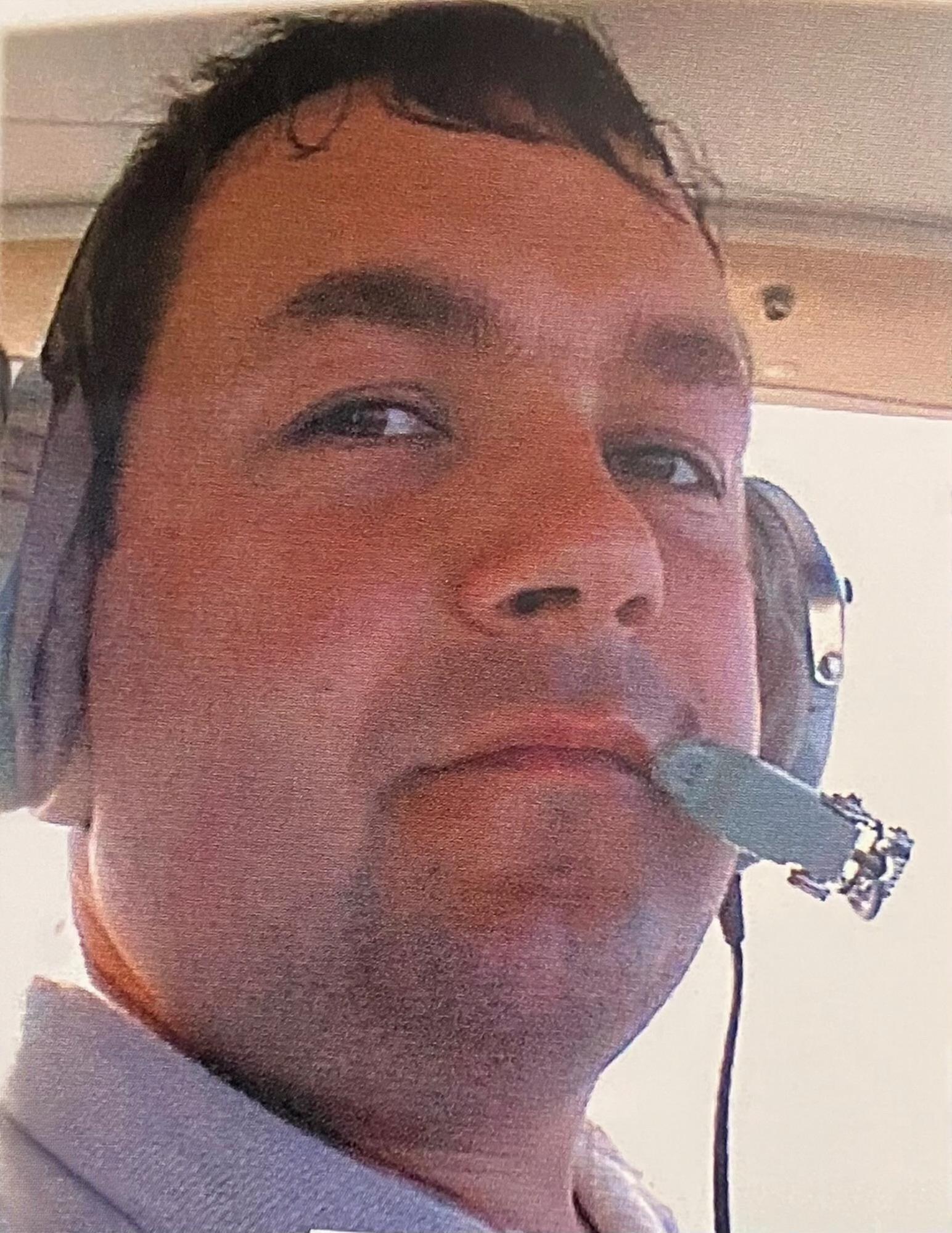 A pilot focuses on the controls while wearing headphones in a small aircraft cockpit.