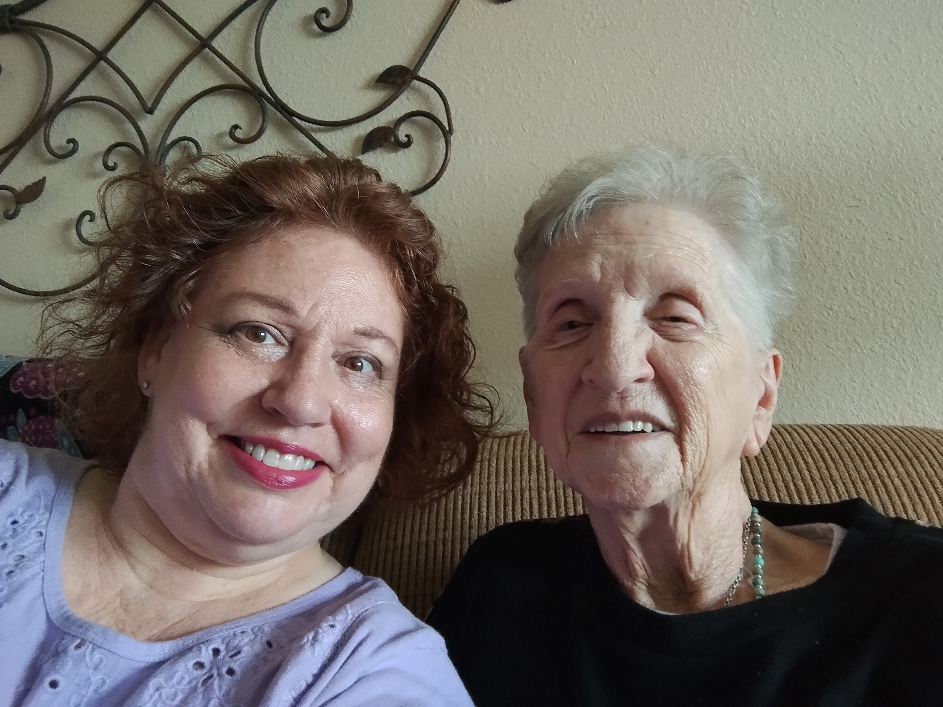 Two women sit close, smiling and enjoying each other's company in a cozy setting.
