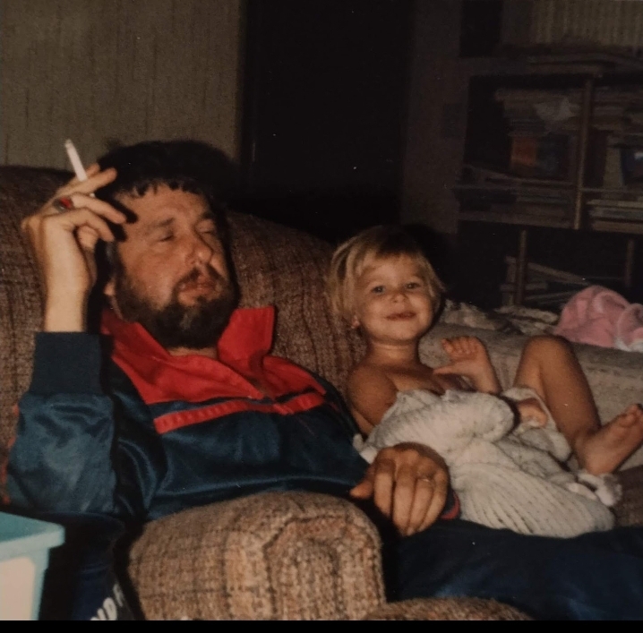 A man and a girl sit together on a couch, enjoying a laid-back moment with a cigarette.
