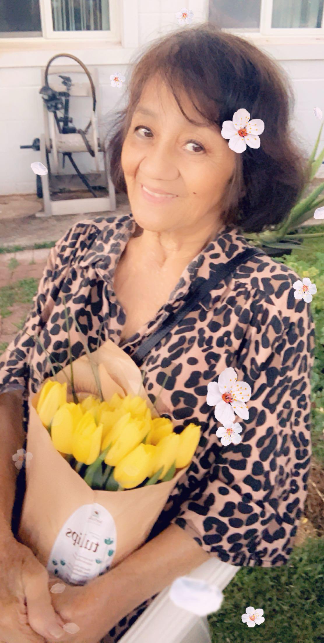 A woman smiles while holding a bouquet of vibrant yellow flowers in a sunny outdoor setting.