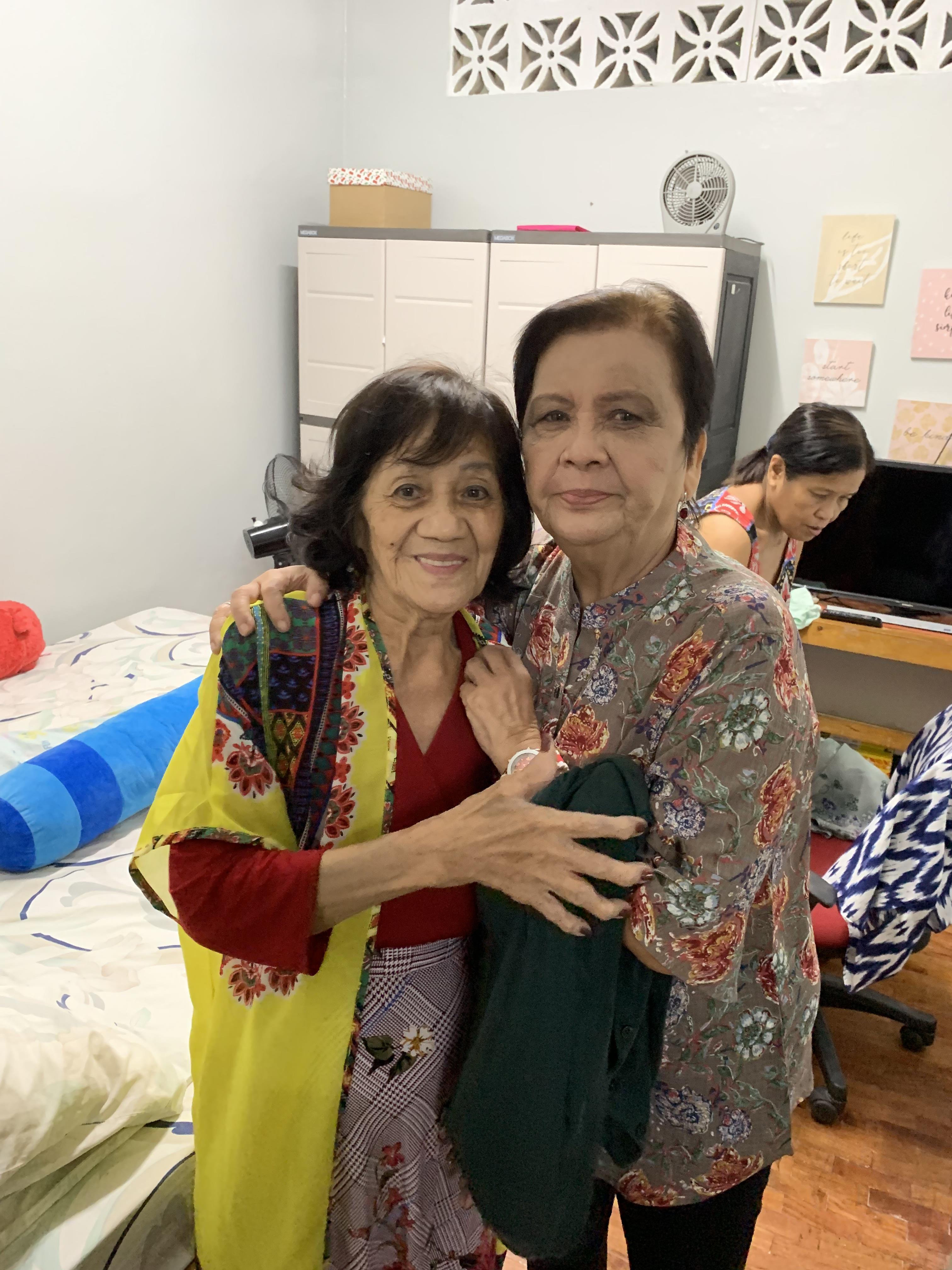 Two women share a heartfelt hug in a comfortable living space while family members mill about.