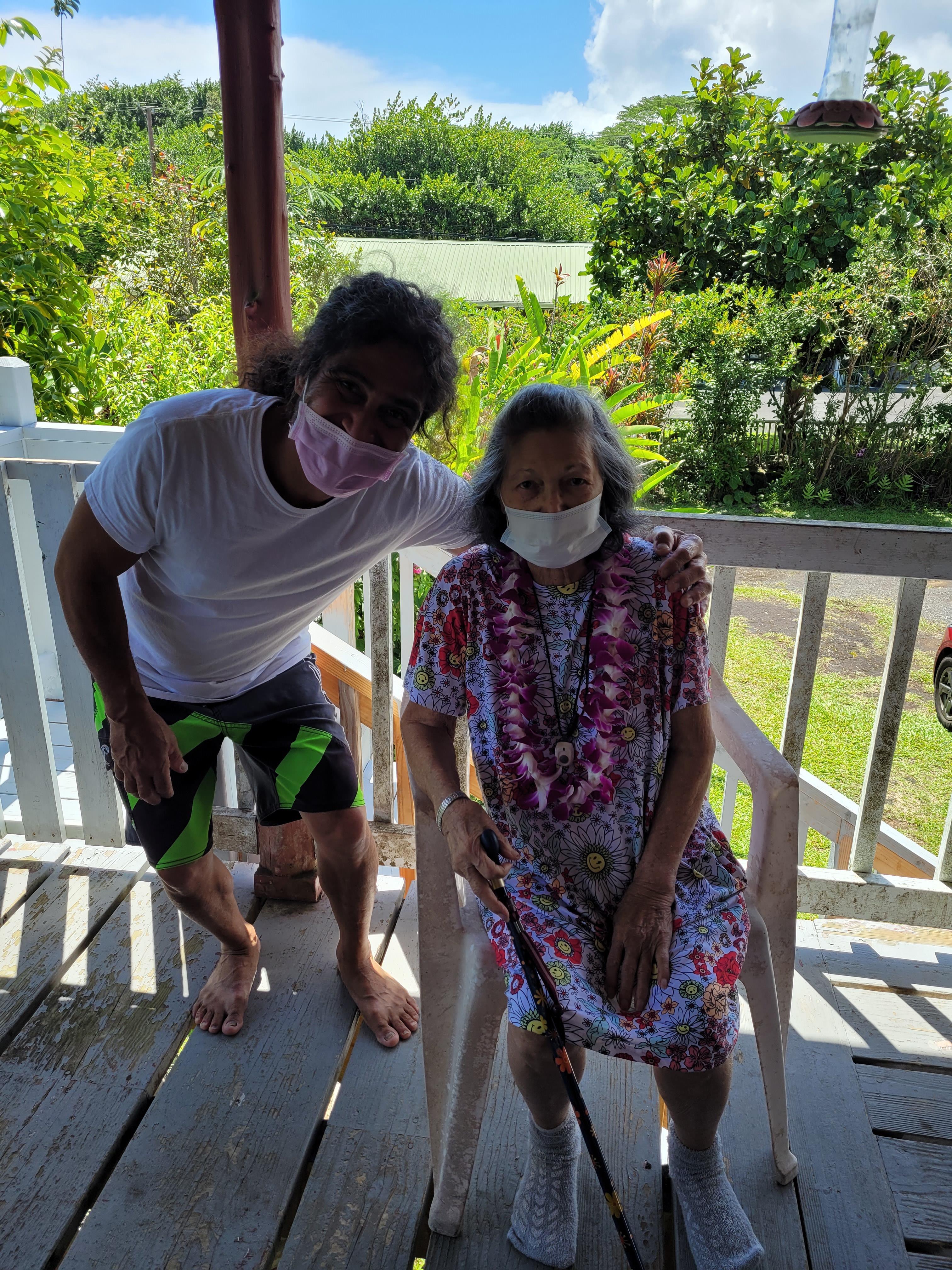 Two family members enjoy their time together outside a house, surrounded by lush greenery.