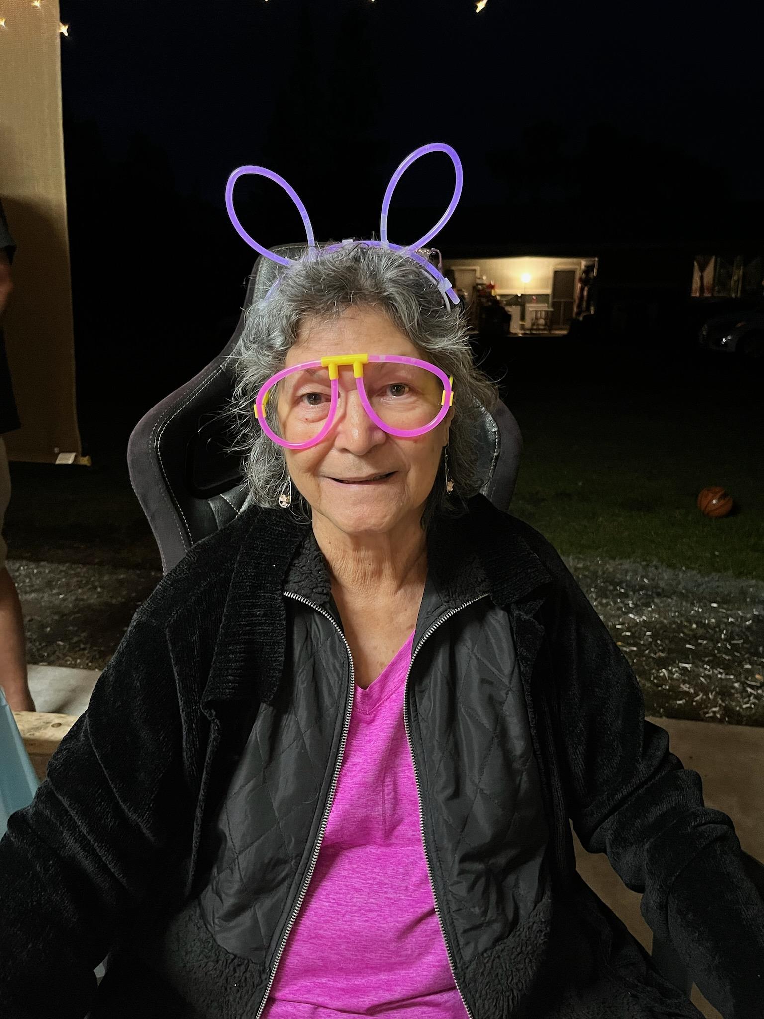 Elderly woman enjoys a joyful backyard gathering wearing colorful accessories with cheerful company.