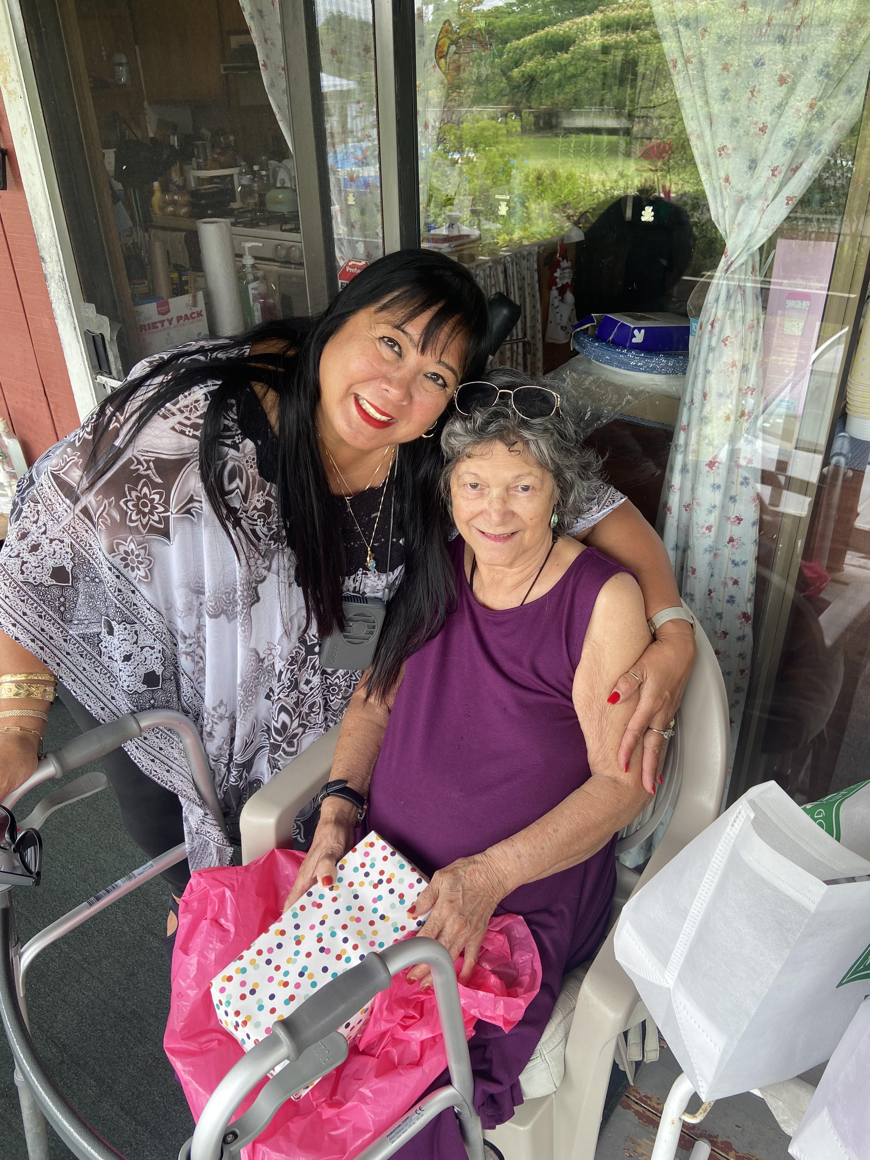 Women are smiling and hugging each other warmly while sitting on a porch together.