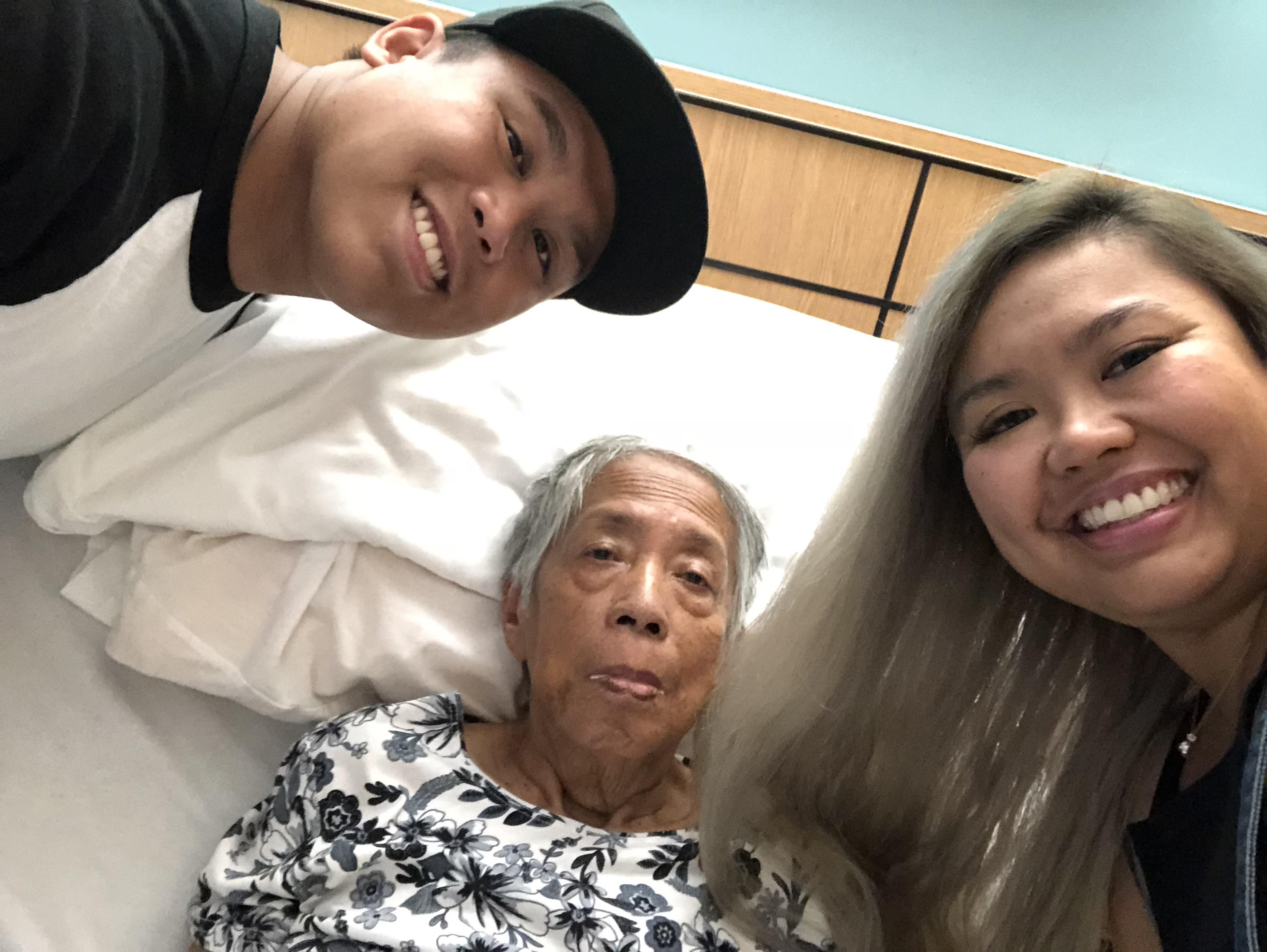 Two relatives joyfully pose with an elderly woman in a hospital room during a loving visit.