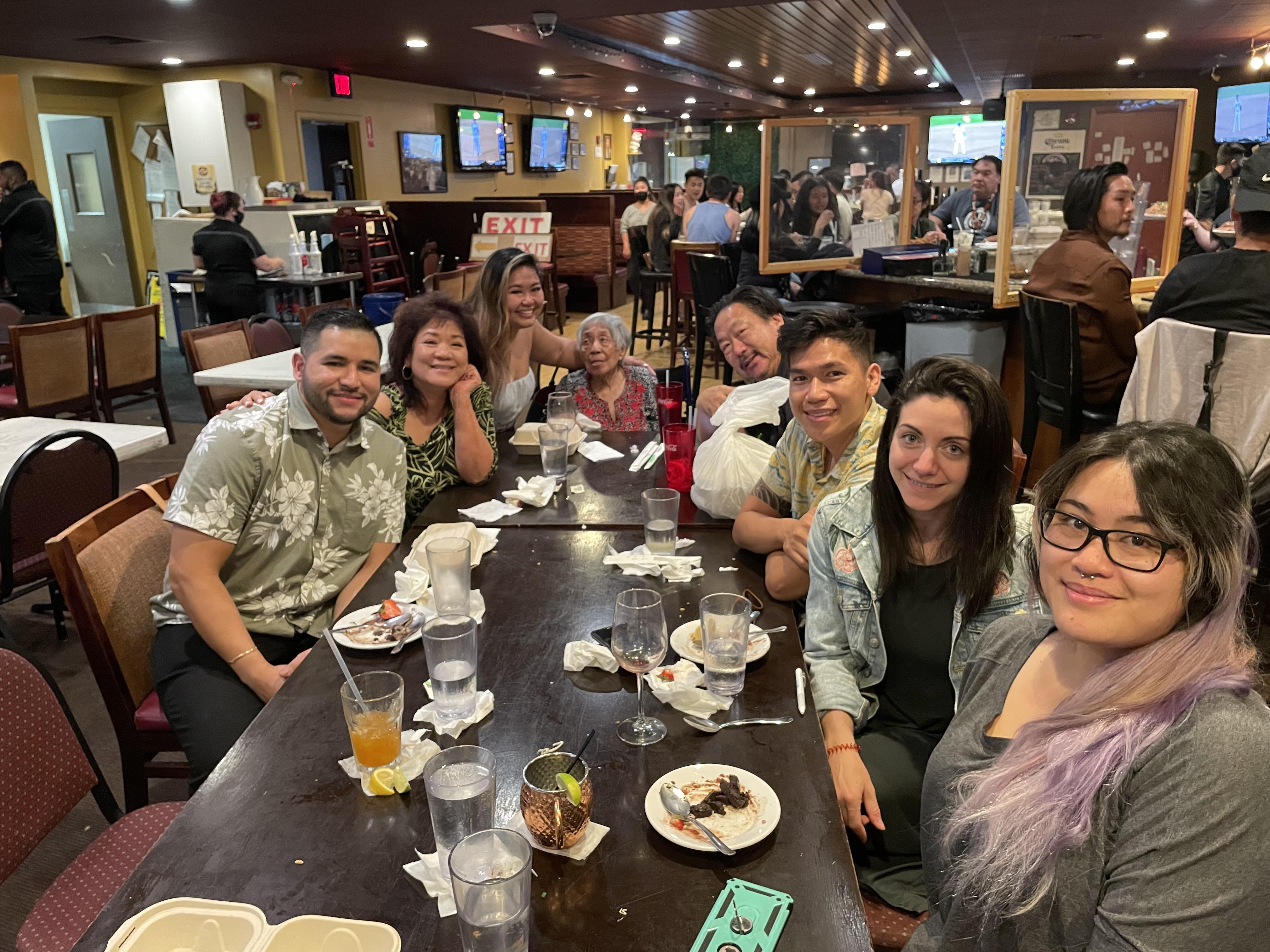 Friends gather around a table enjoying food and drinks while chatting at a restaurant.