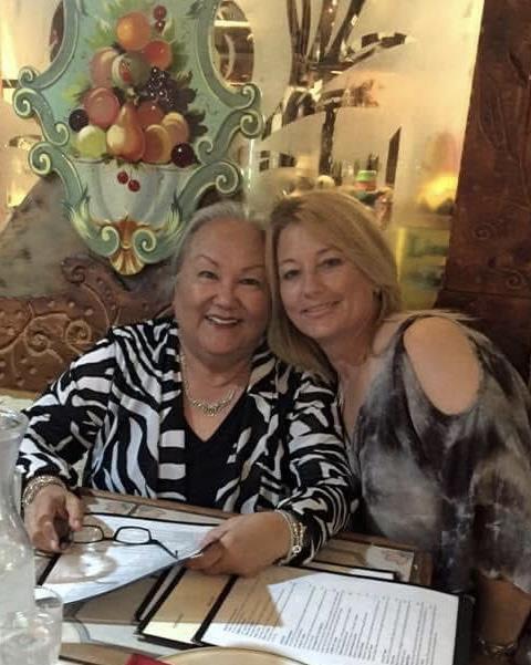 Two women share smiles while seated at a restaurant table, surrounded by colorful decor.