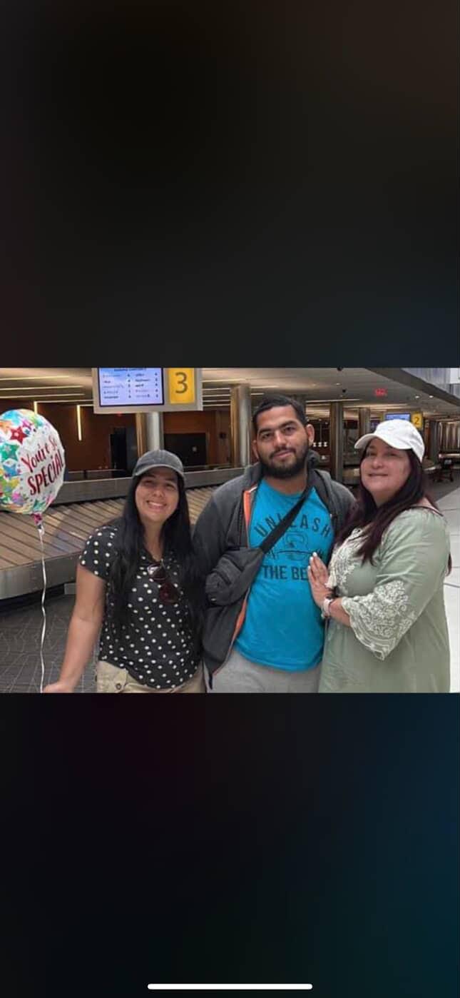 Friends gather joyfully at the airport to celebrate a reunion, holding a balloon and smiling.
