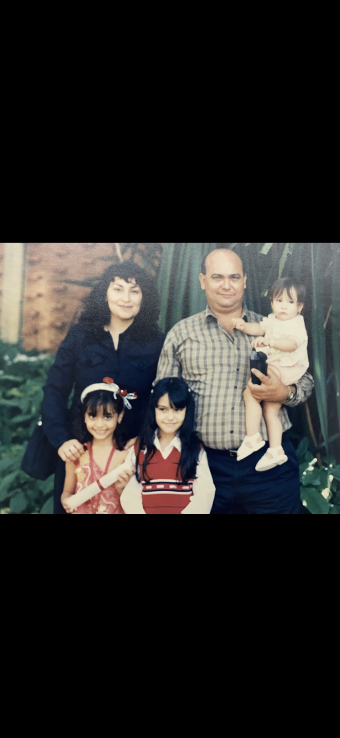 A family stands together in a garden, smiling and enjoying a sunny afternoon with their children.
