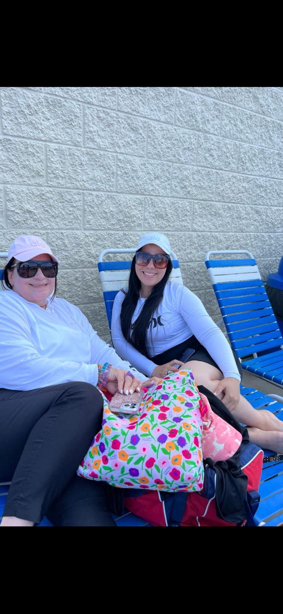 Two friends sit comfortably by the pool, soaking up the sun on a cheerful day.