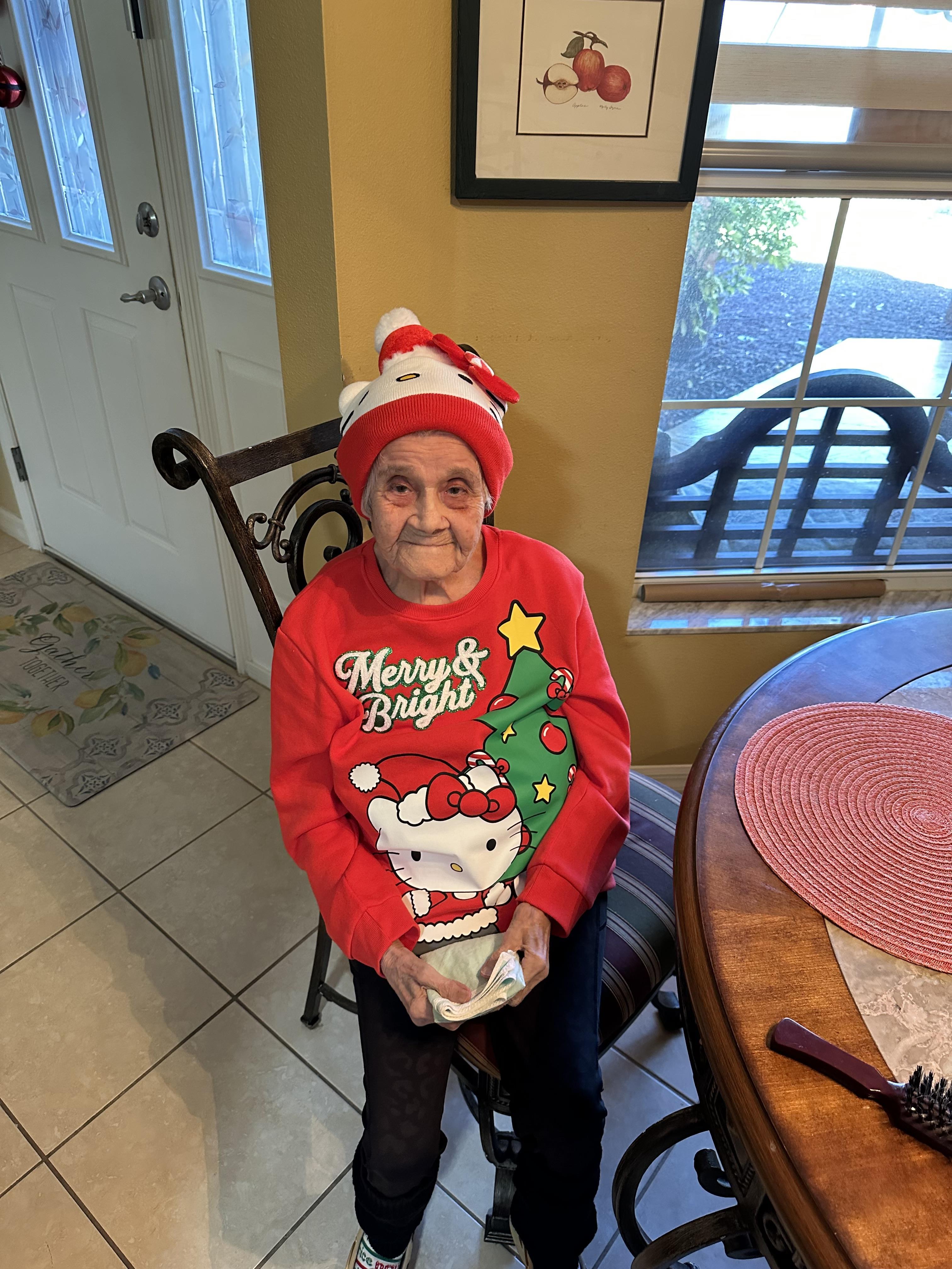 Elderly person in a Christmas sweater and hat sits joyfully at a decorated dining table.