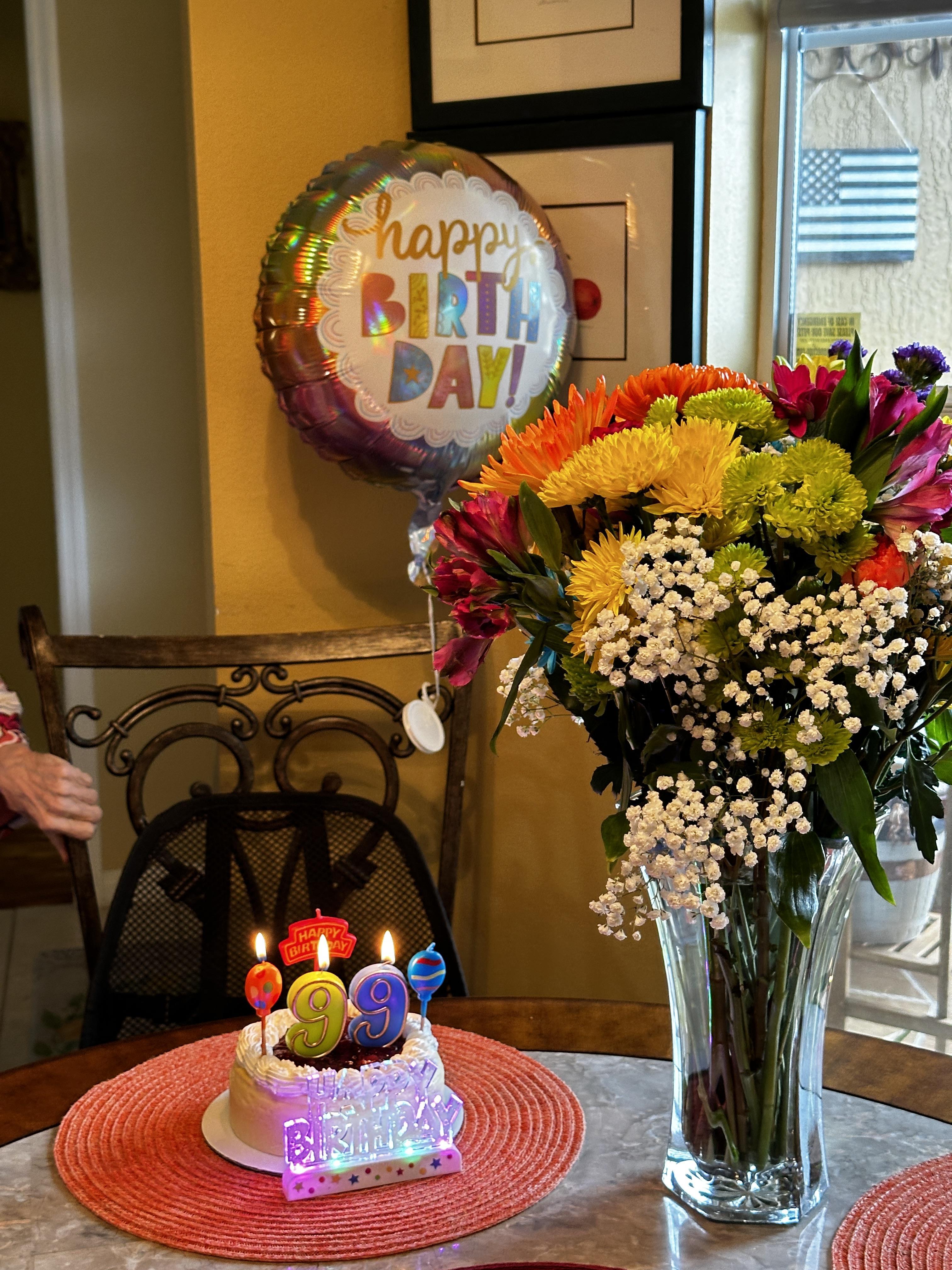 A birthday celebration with a cake, candles, flowers, and balloons in a cozy room.