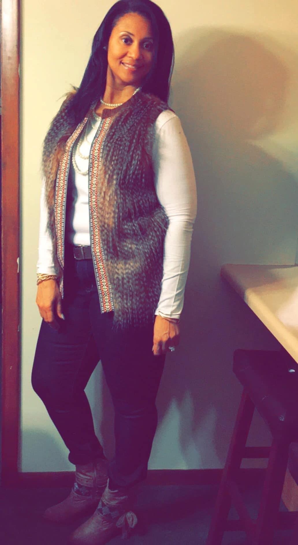 Woman stands confidently indoors wearing a cozy sweater vest and stylish outfit.