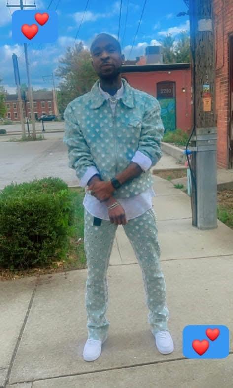 A man stands on a city sidewalk wearing a stylish patterned denim outfit, exuding confidence.