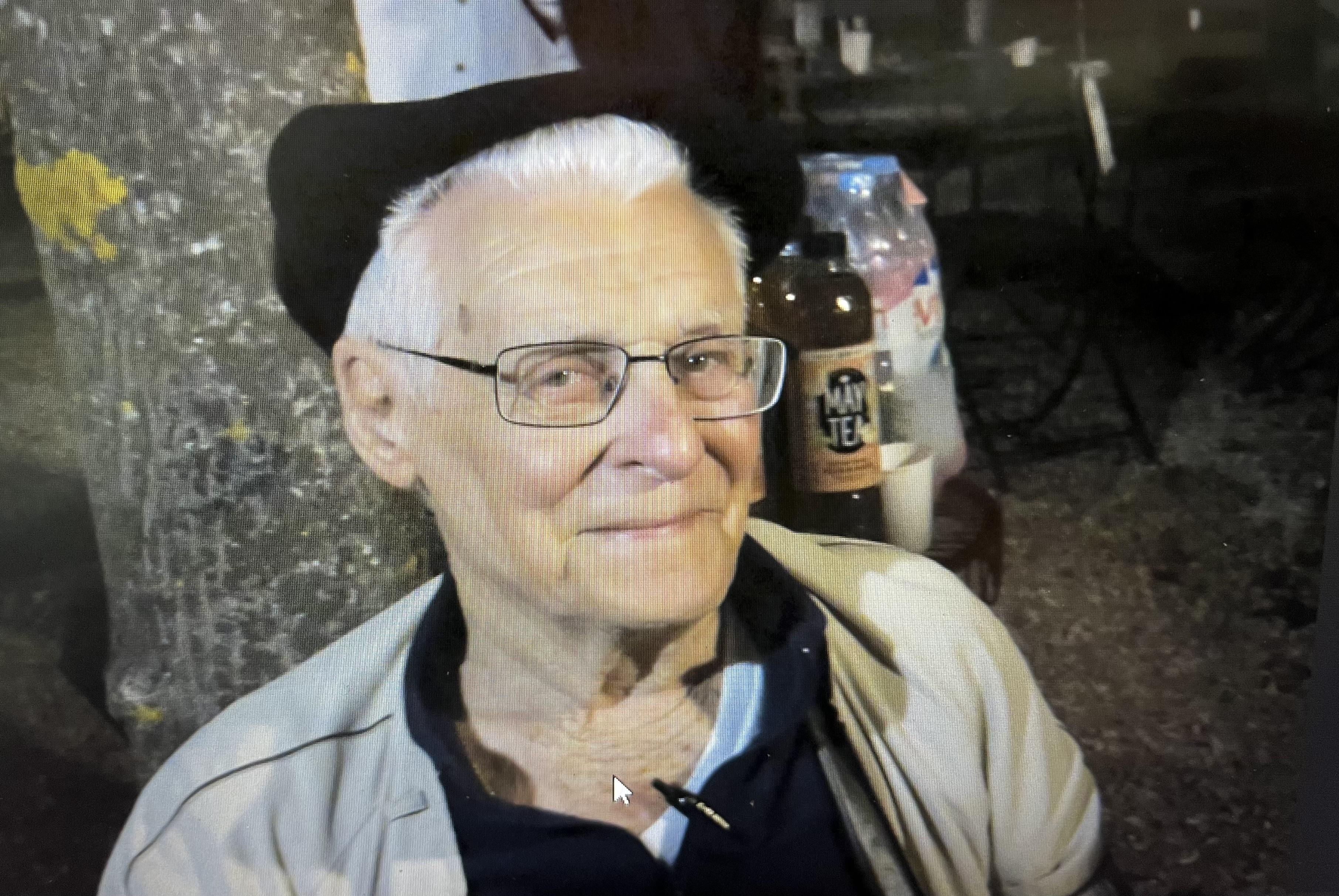 An elderly gentleman wearing glasses and a hat enjoys a relaxed evening outdoors, smiling gently.