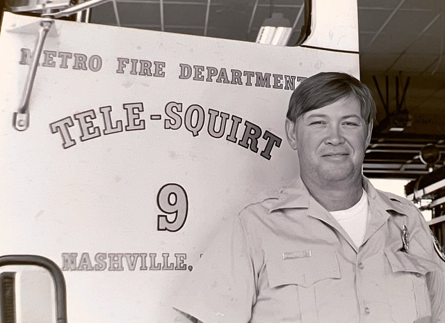 A firefighter stands proudly by a vintage fire truck, reflecting on years of service in Nashville.