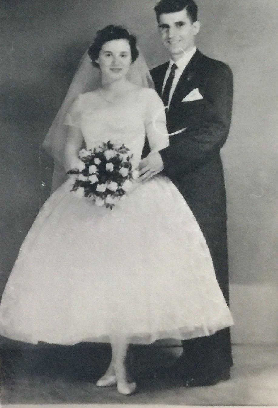 Couple poses together in elegant wedding attire with bouquet, radiating joy and commitment.