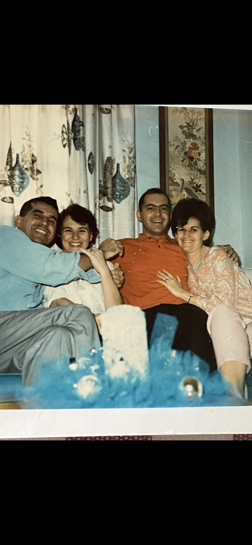 Four friends smile and share joyful moments while sitting on a sofa surrounded by colorful decor.