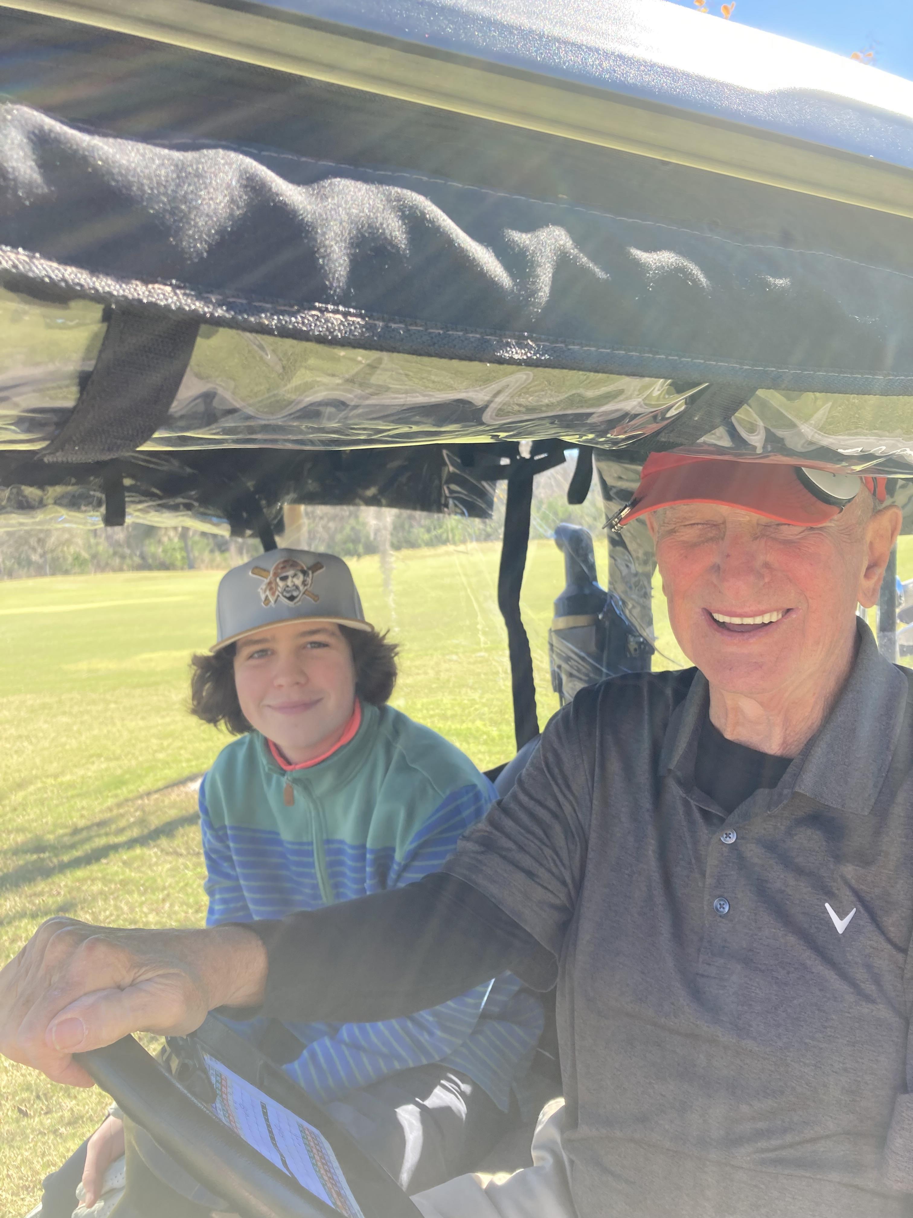 Two golfers relax in a golf cart, smiling and enjoying their time on the sunny golf course.