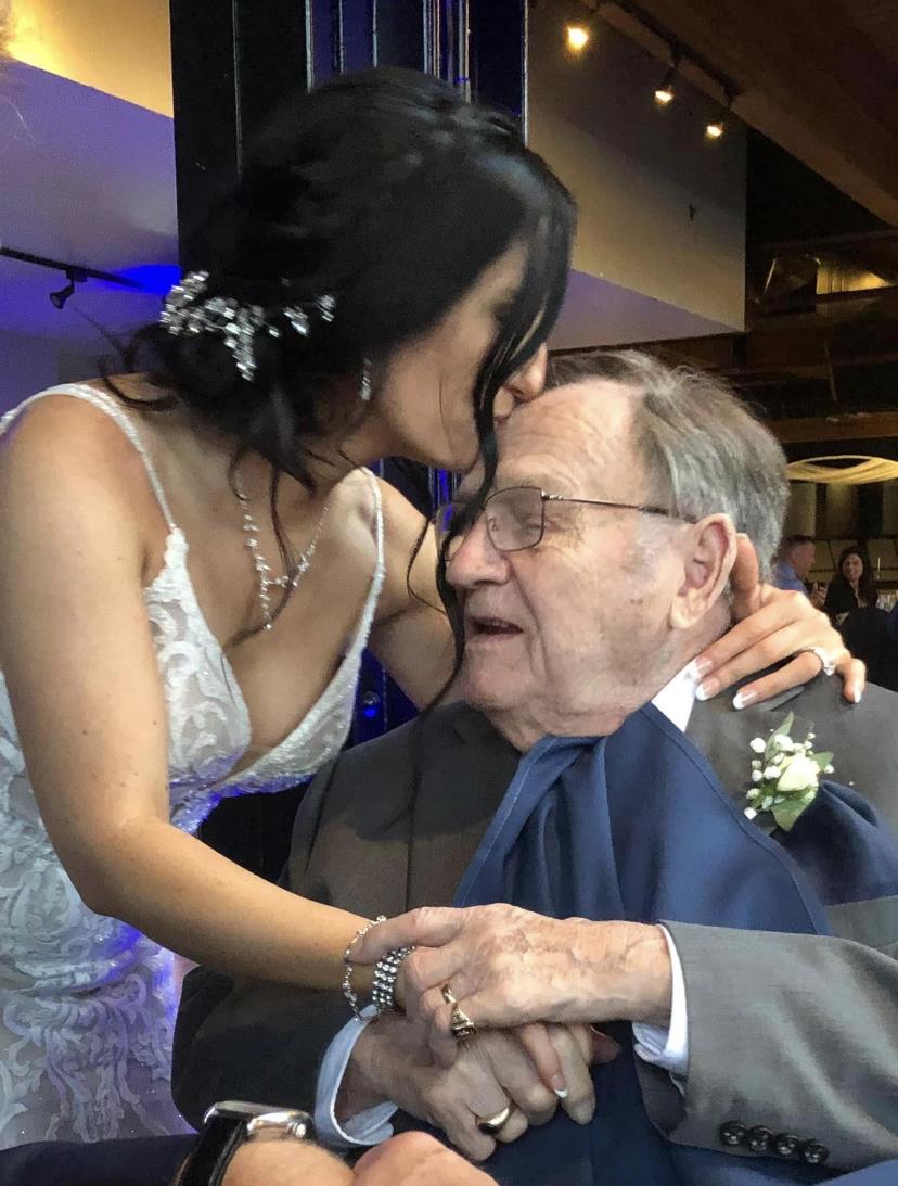 A bride shares a tender kiss on her grandfather's cheek at a wedding reception, showcasing love.