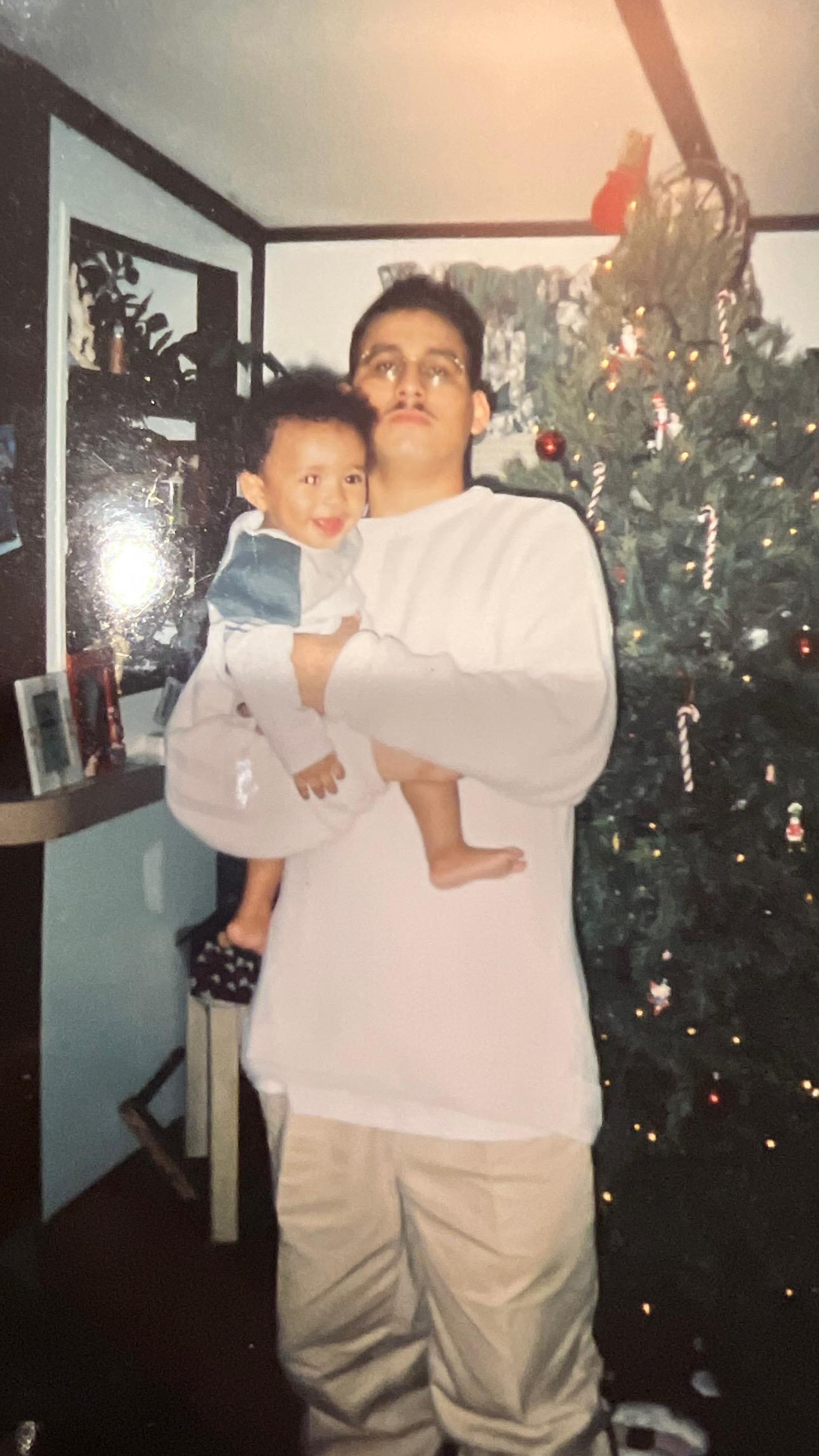 A joyful person holds a smiling child in front of a beautifully adorned Christmas tree.