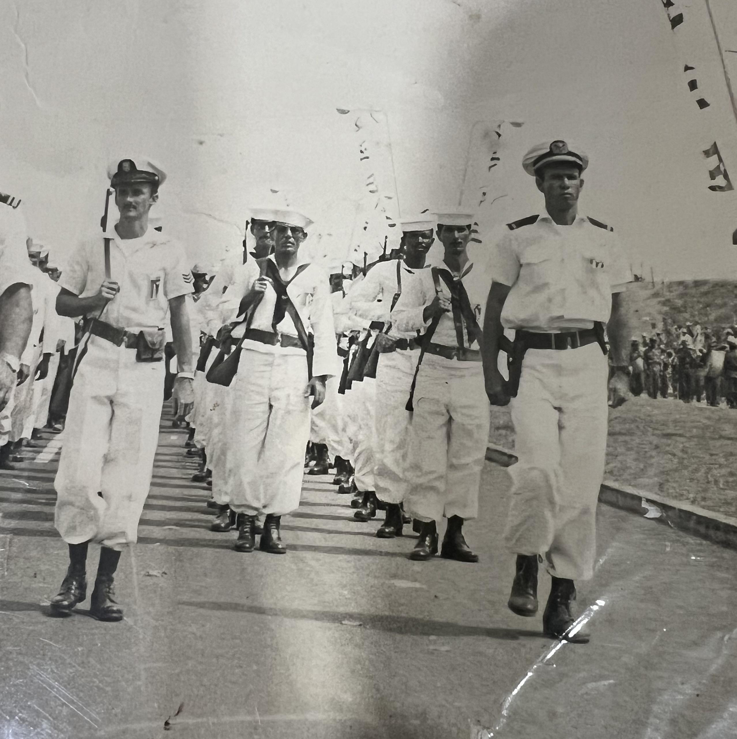 Sailors in white uniforms march in formation, displaying discipline and teamwork at a ceremony.
