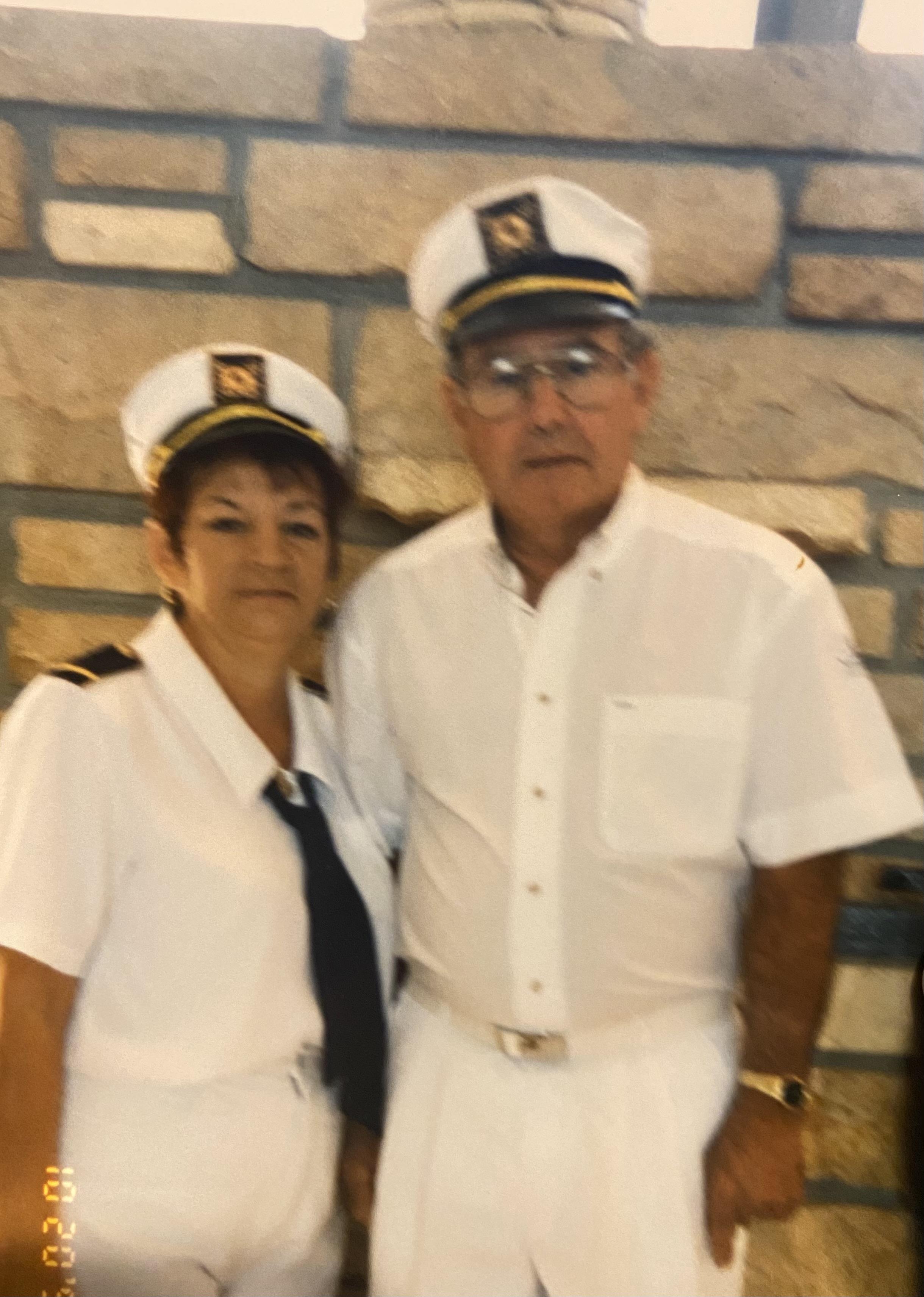 A couple in matching white nautical uniforms smiles together in a warmly lit room.