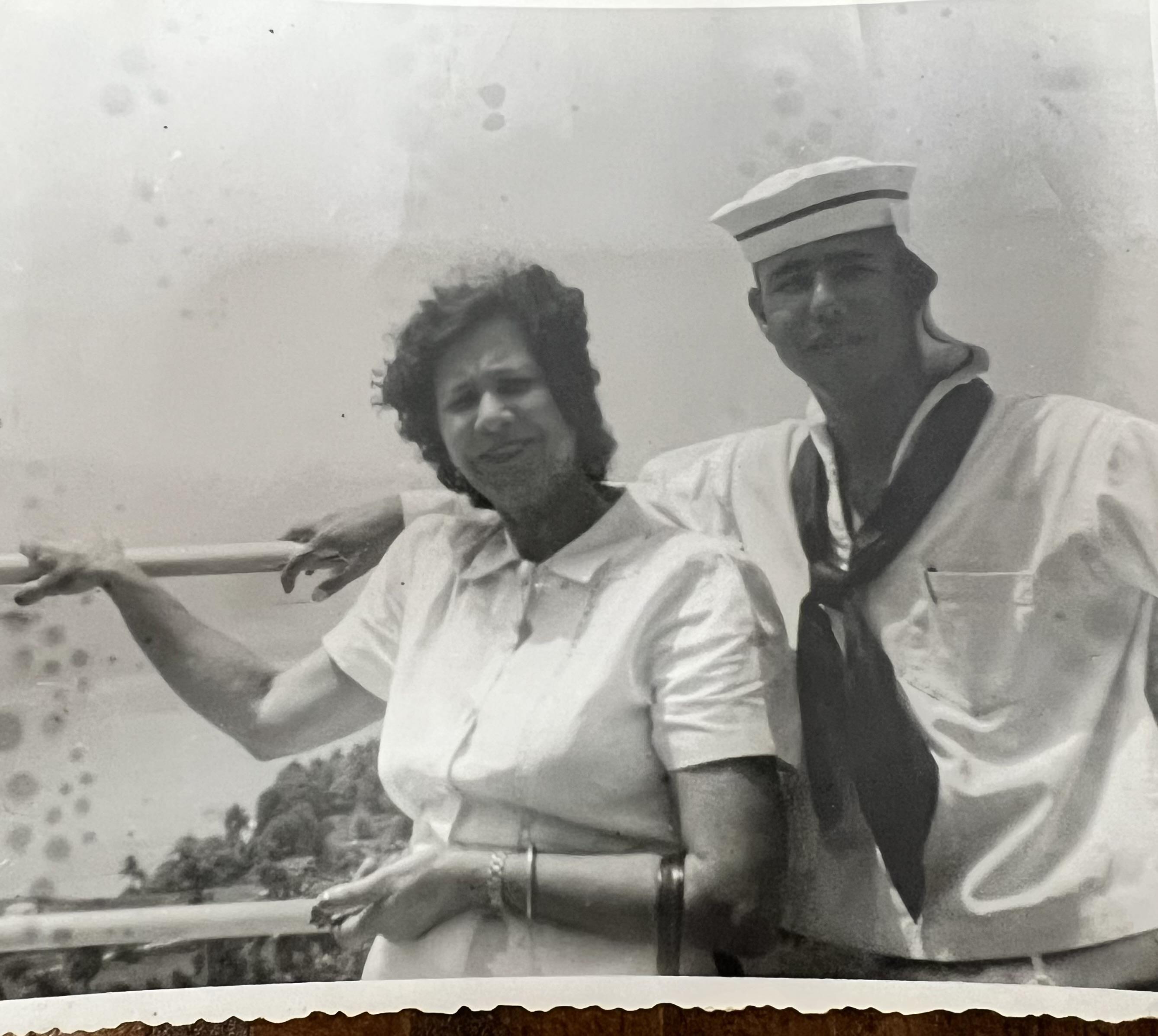 A couple poses on the deck of a boat, enjoying a sunny day at sea, dressed in vintage attire.