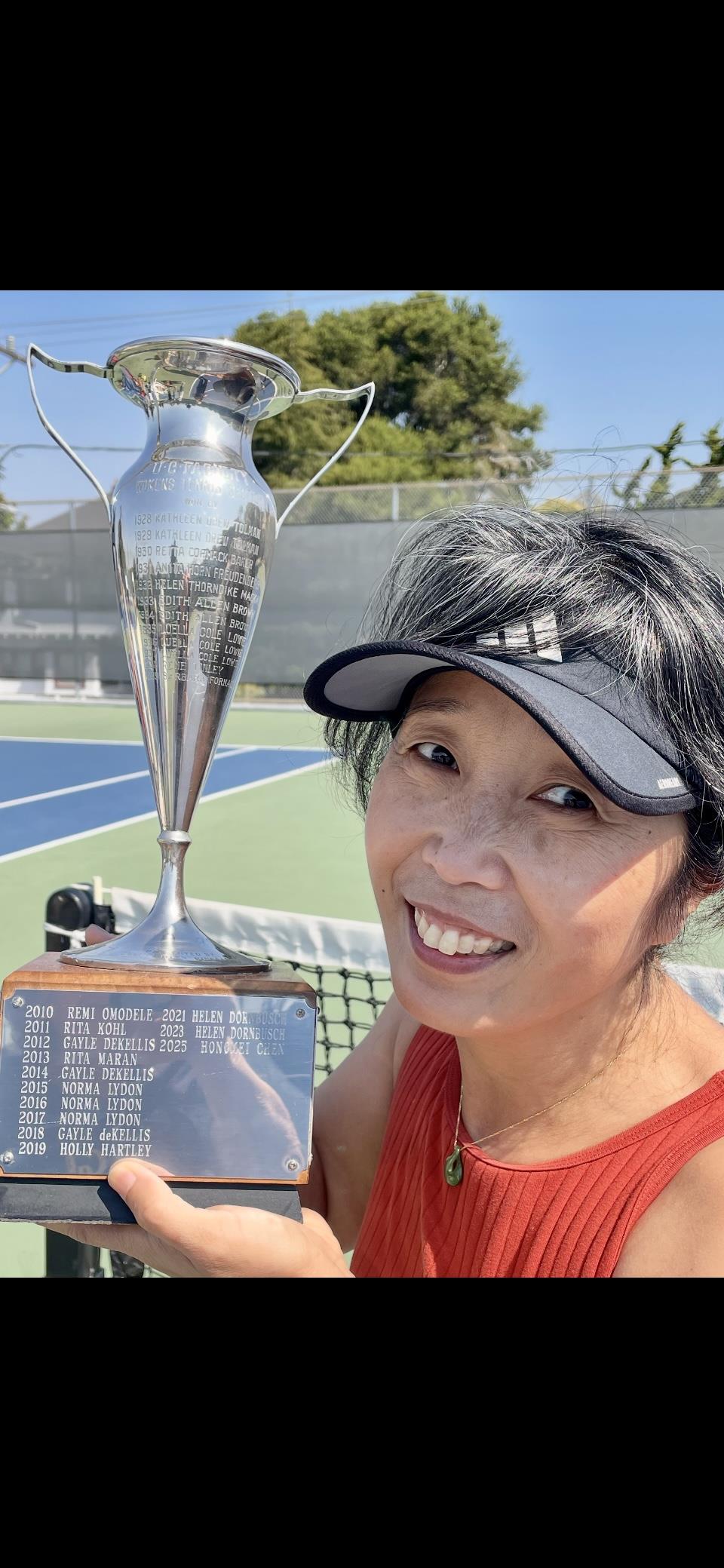 A tennis player beams with pride, holding a trophy after winning a local tournament.