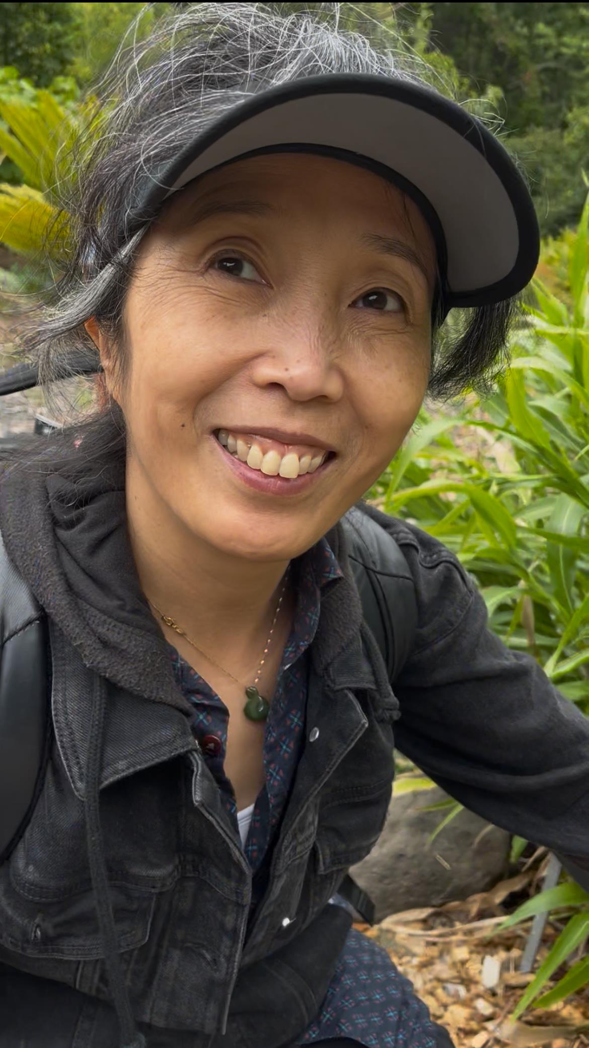 A woman enjoys her time in a vibrant garden, surrounded by greenery, smiling warmly at the camera.