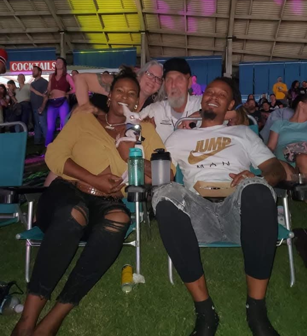 Four friends share laughter and food at a vibrant outdoor festival on a lively night.