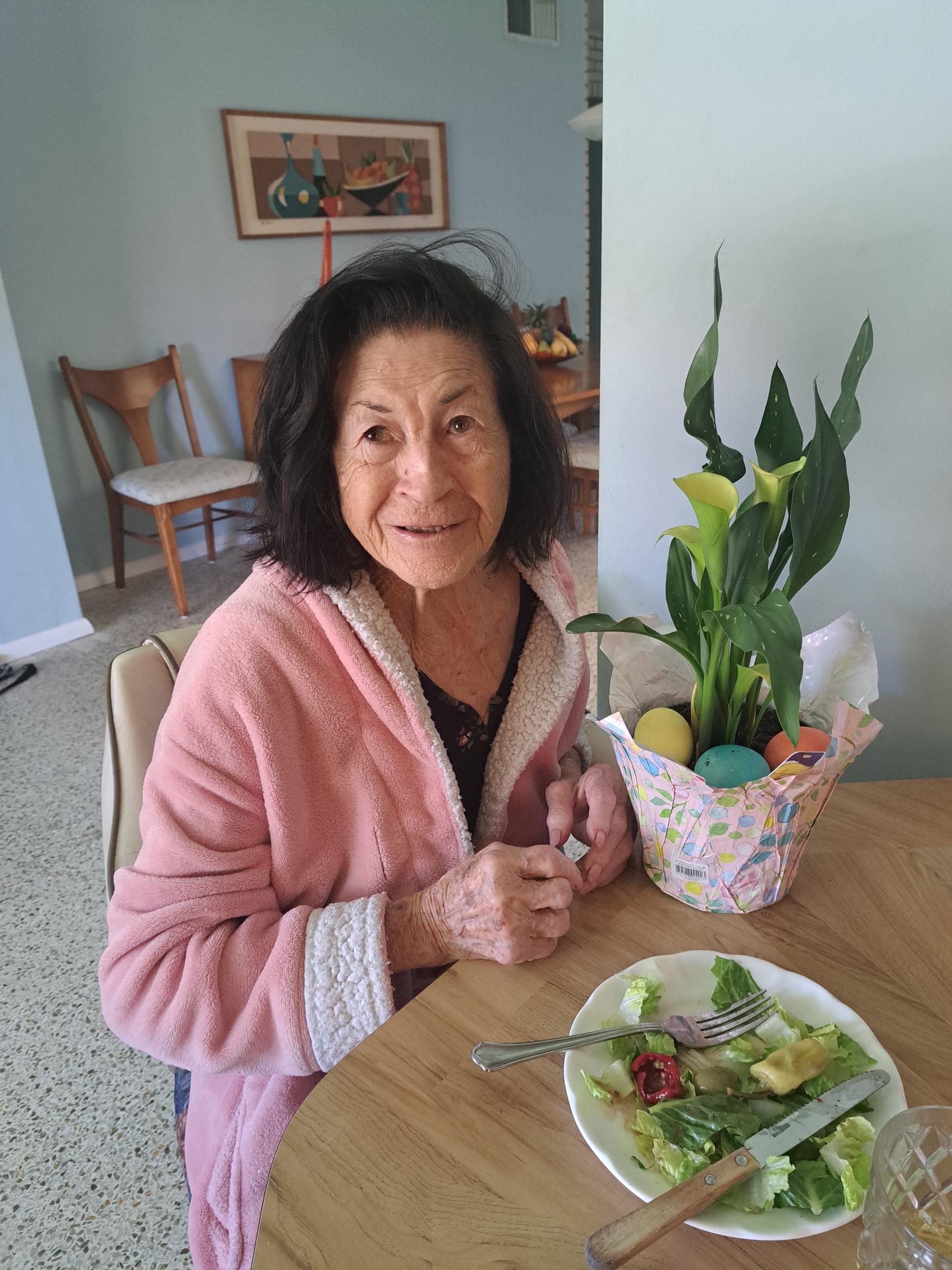 An older woman smiles while having a salad at her dining table with spring decorations nearby.