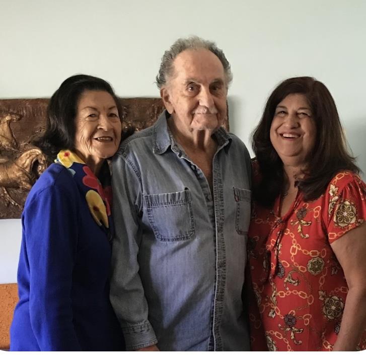 Three individuals embrace in a relaxed indoor atmosphere, sharing happiness and connection.