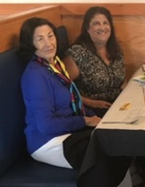 Two women relax at a restaurant booth, sharing conversation and enjoying their food.