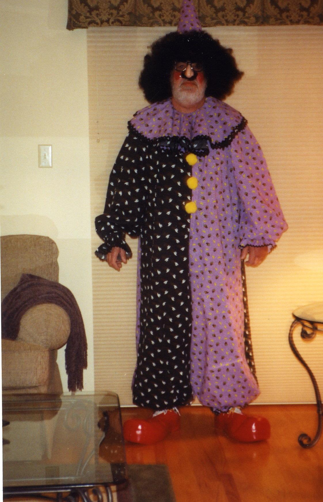 A clown stands confidently in a playful outfit with distinctive colors and patterns in a warm room.